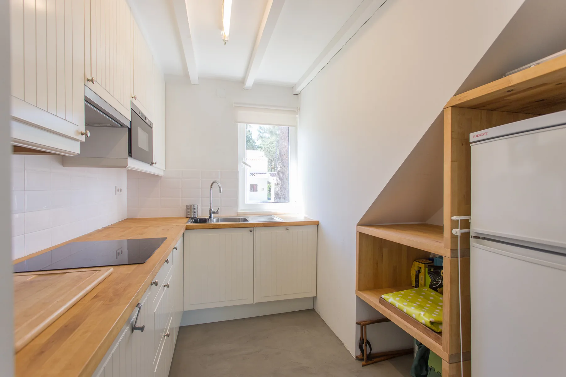 Una cocina estrecha con armarios claros, encimeras de madera y una ventana sobre el fregadero.