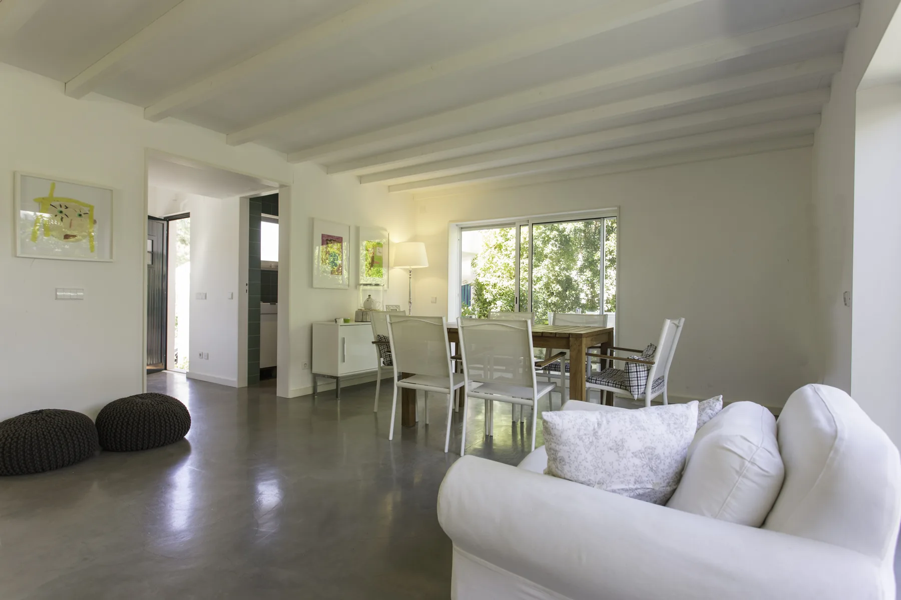 Una luminosa sala de estar y comedor con asientos blancos y una mesa junto a la ventana.
