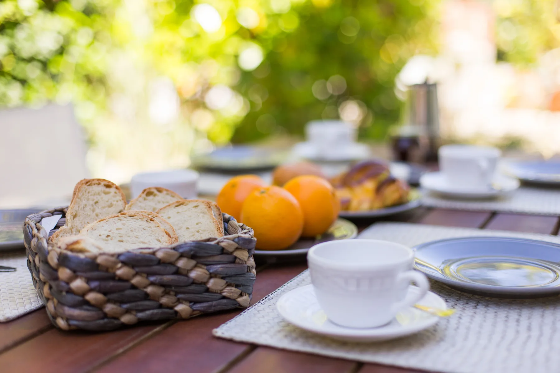 Una mesa de desayuno al aire libre con pan, fruta y tazas.