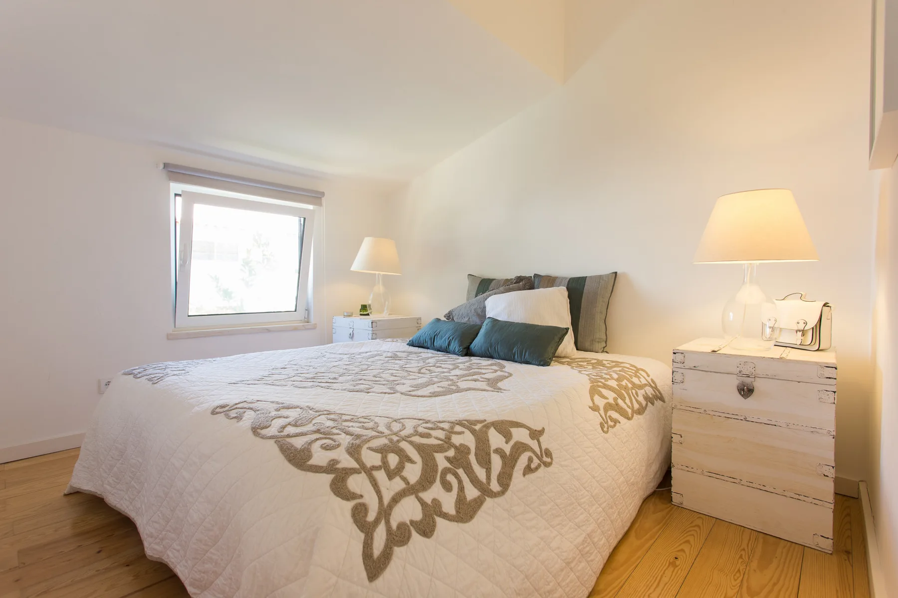 Un dormitorio luminoso con una cama, lámparas de noche y una ventana.
