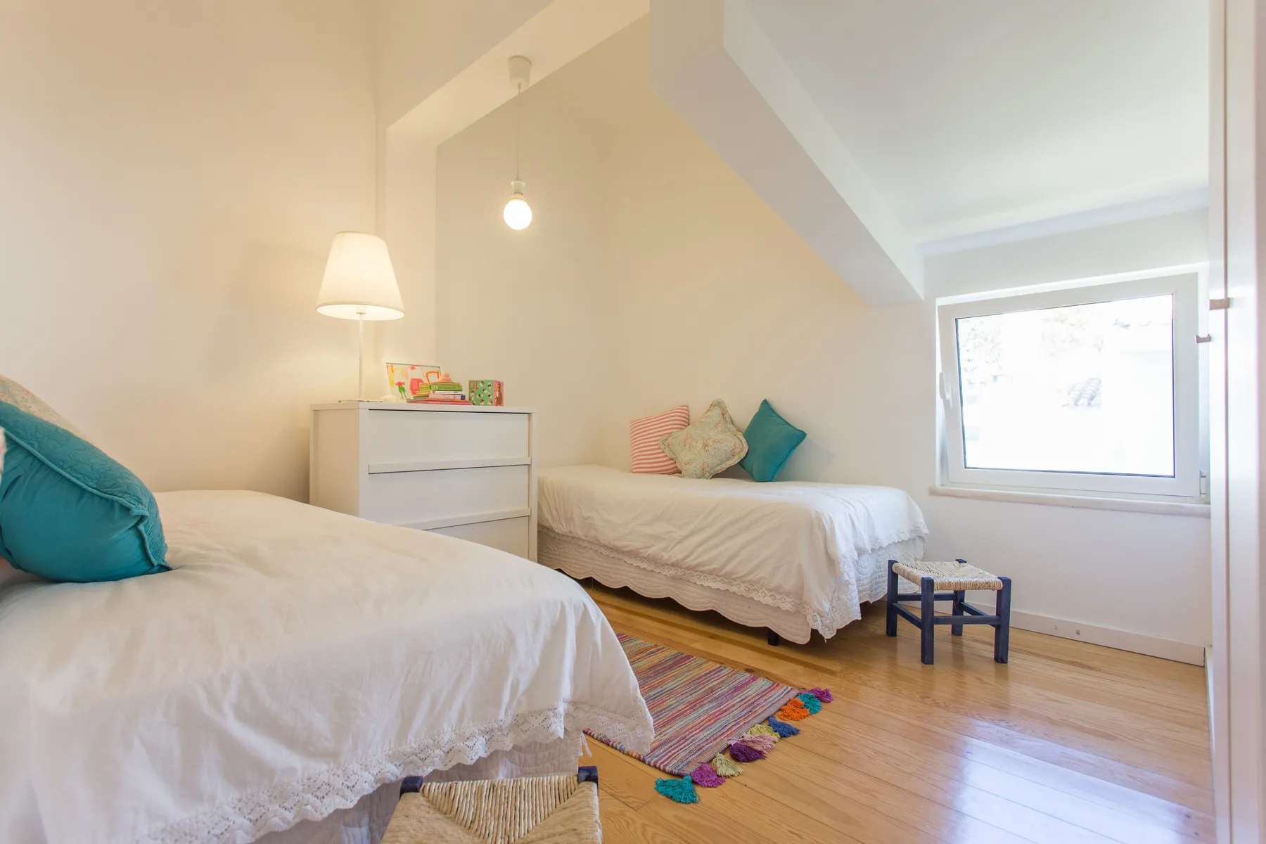 Un dormitorio luminoso con dos camas, una cómoda y una ventana.