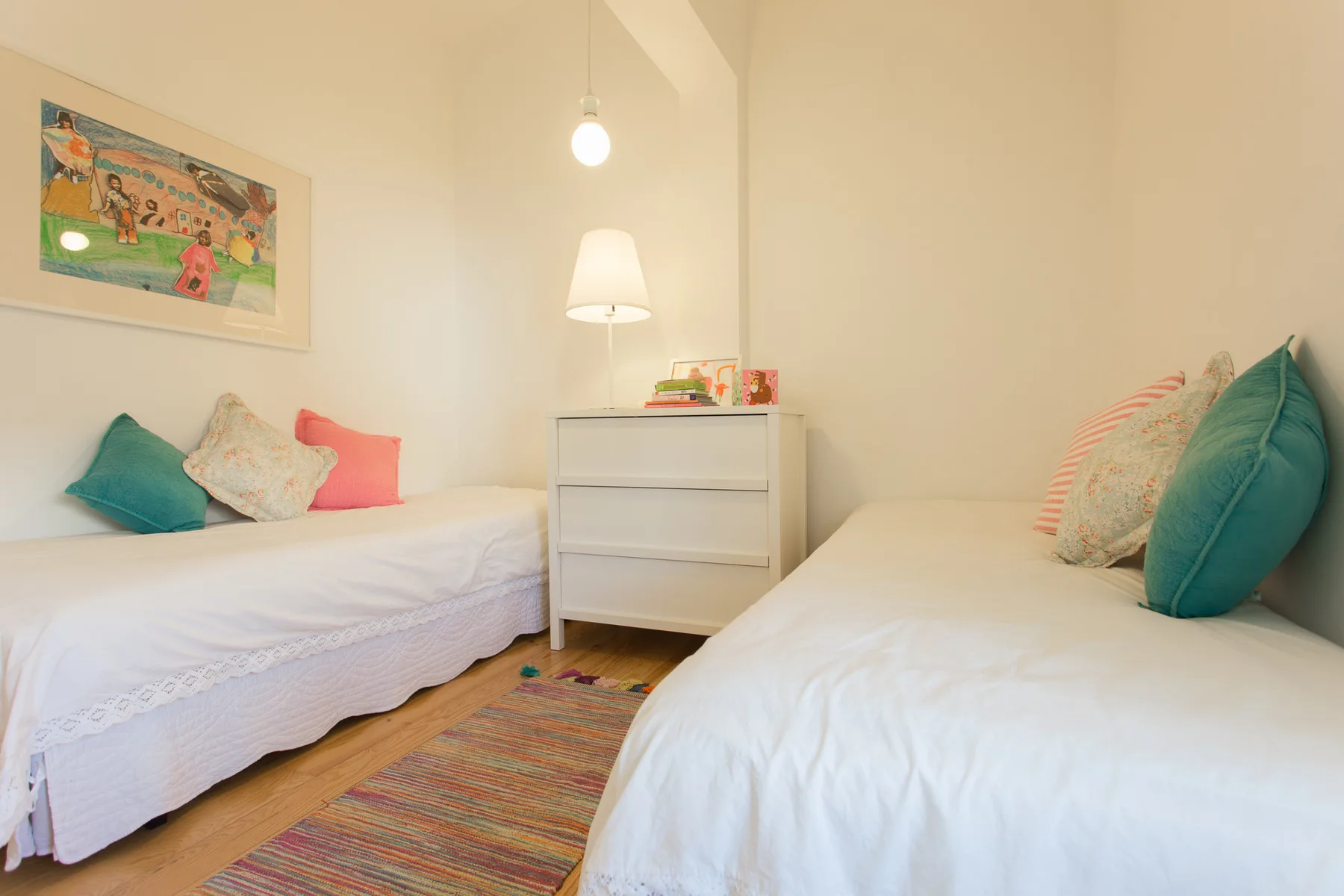 Un dormitorio con dos camas individuales, una mesita central y arte colorido en la pared.