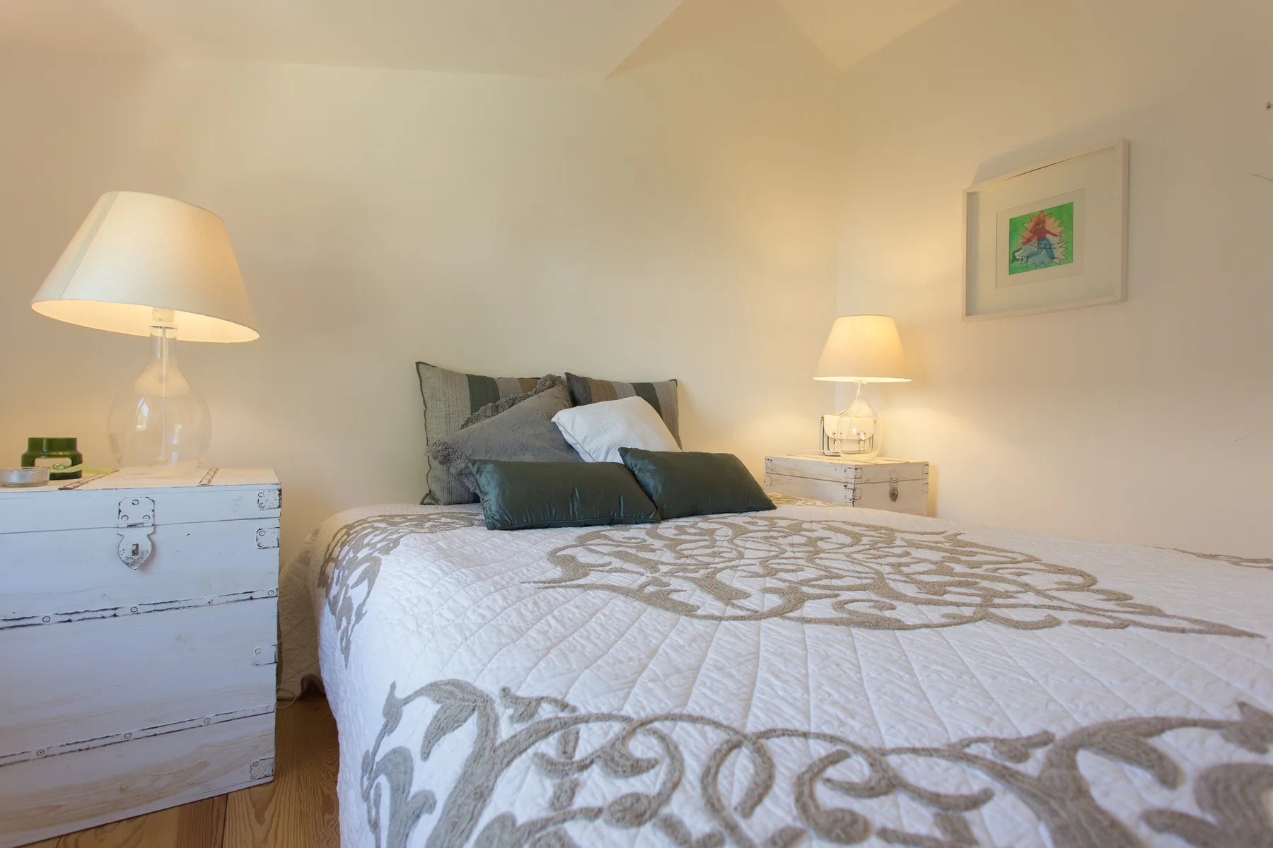 Un dormitorio con una cama tendida, lámparas de mesilla y un cuadro enmarcado.
