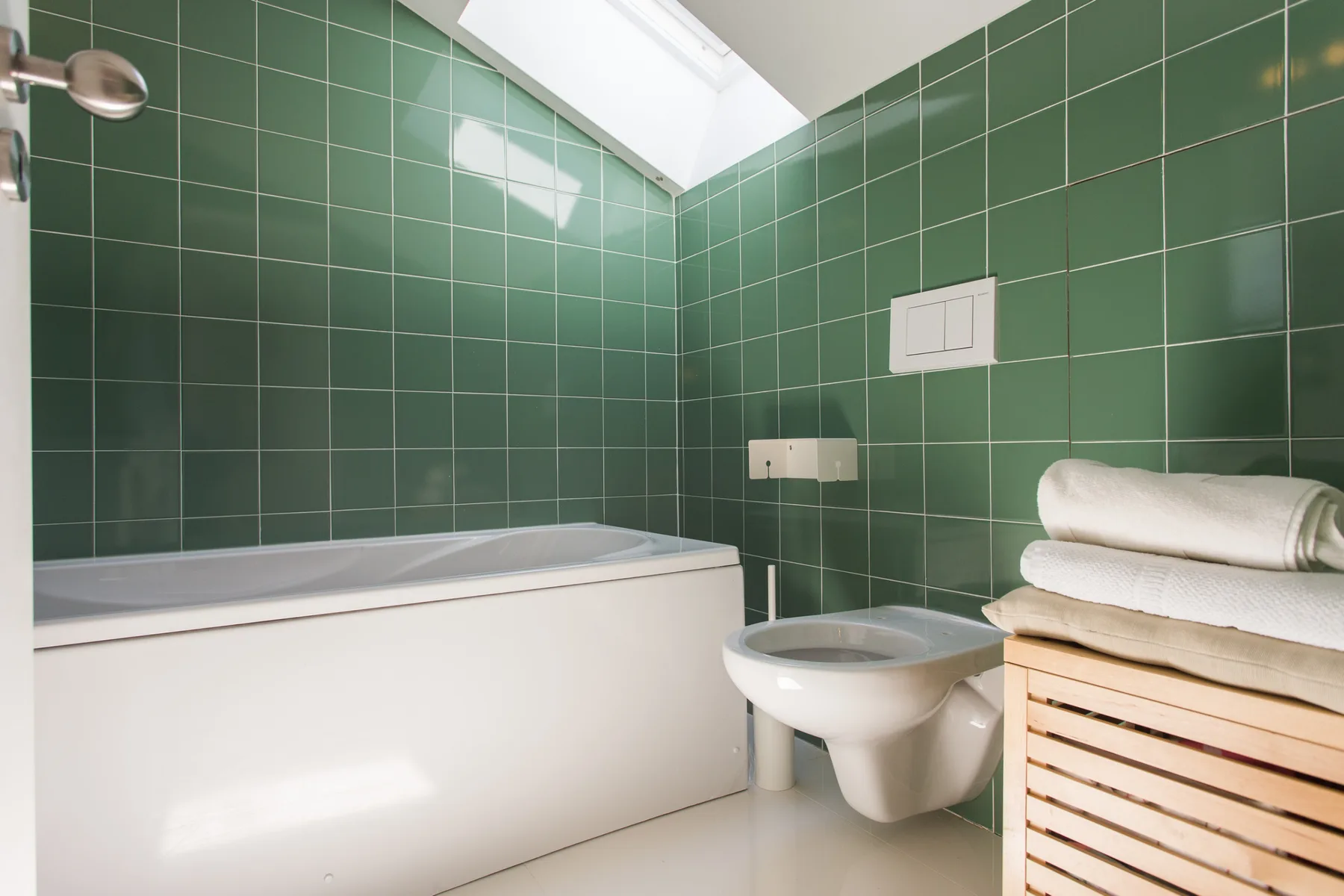 Un baño con paredes de azulejos verdes, bañera y lavabo.