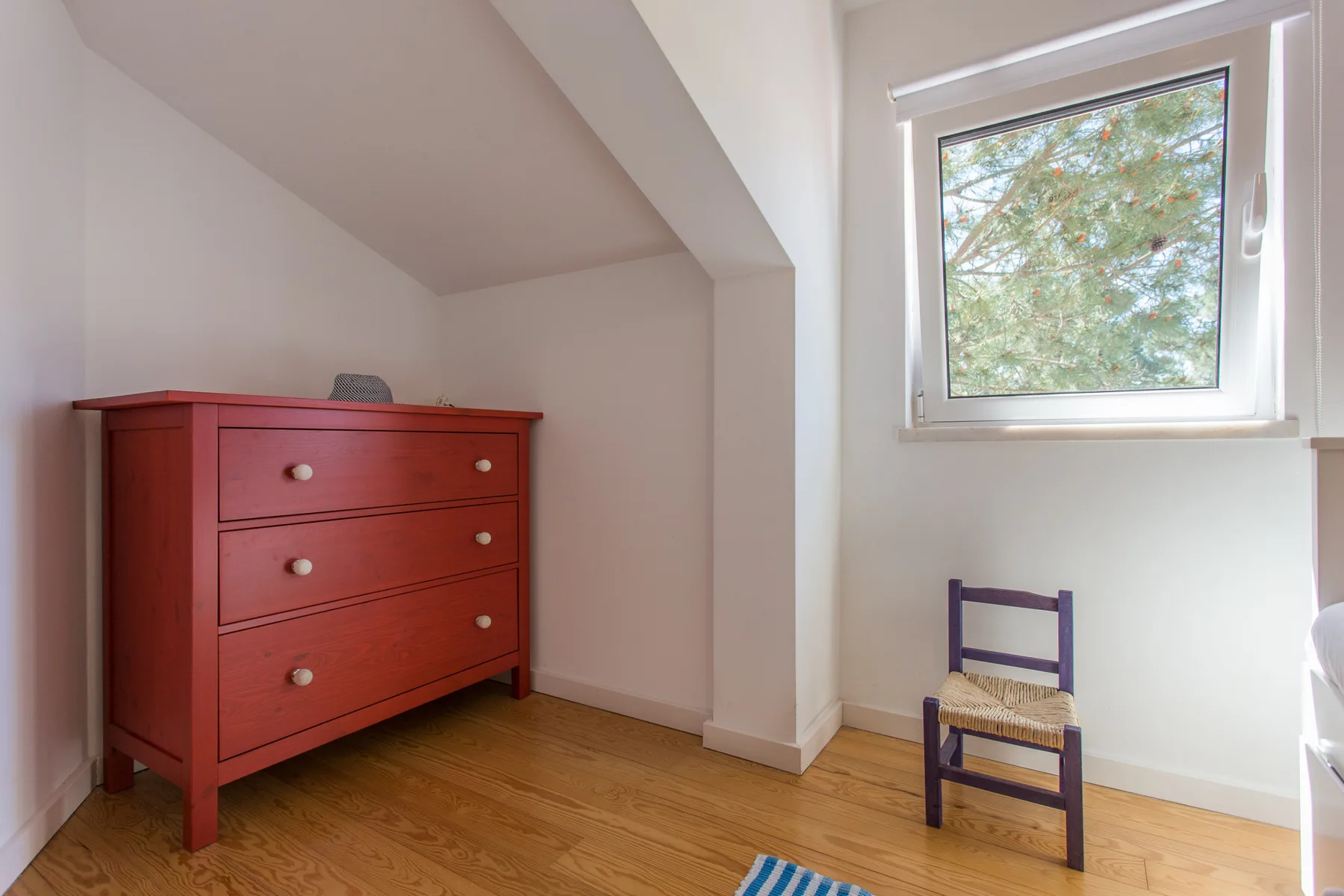 Una habitación luminosa con una cómoda roja, suelo de madera y una ventana.