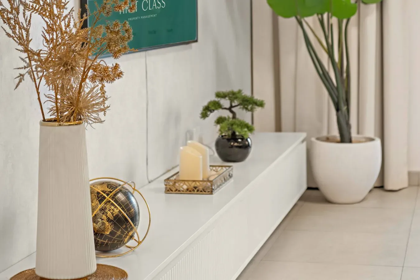 A bright interior display features a white console with plants and decorative objects.