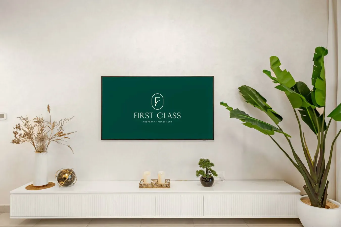 A bright room features a long white cabinet, decorative plants, and a framed sign.