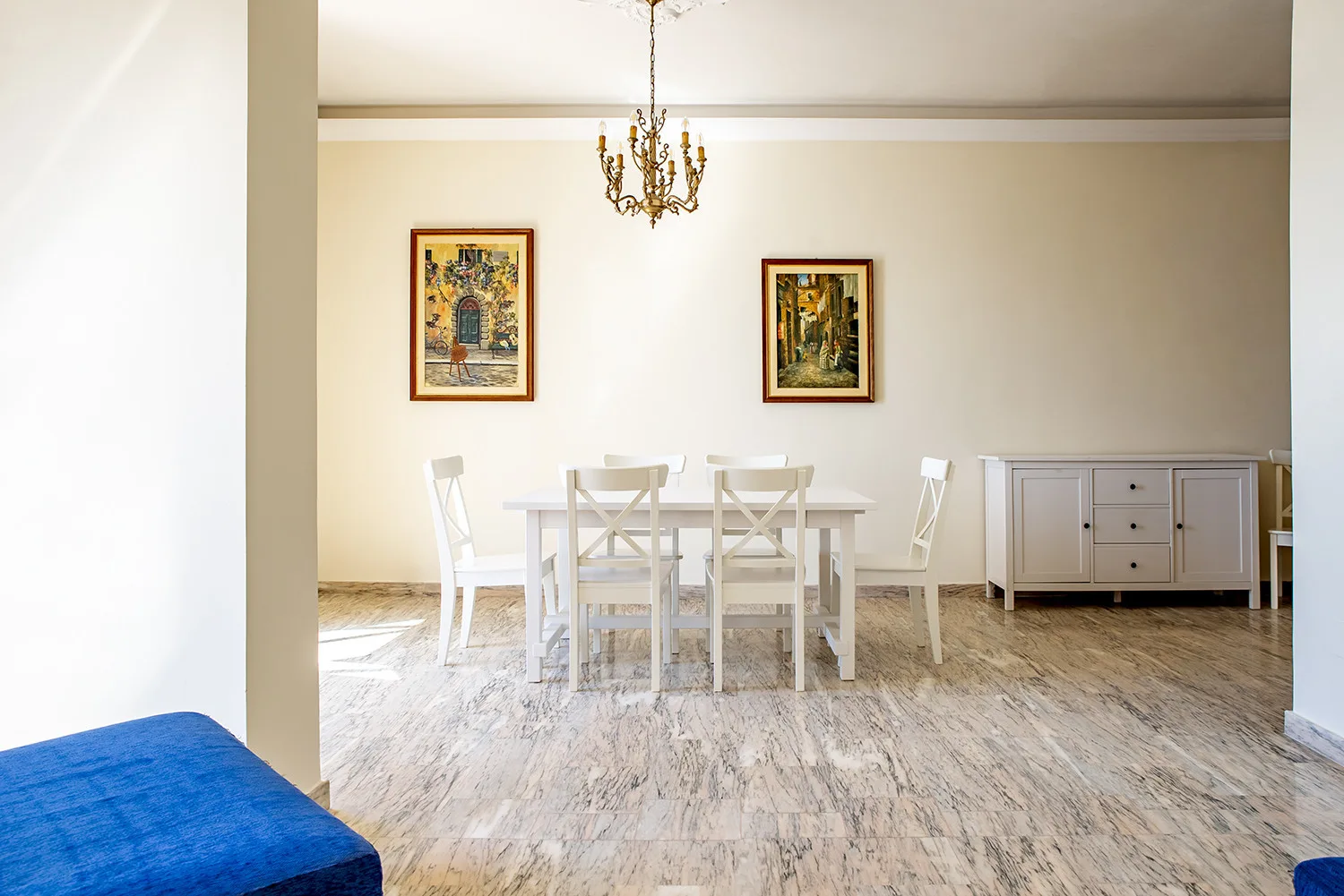 Un comedor luminoso con una mesa blanca y sillas bajo una lámpara de araña.
