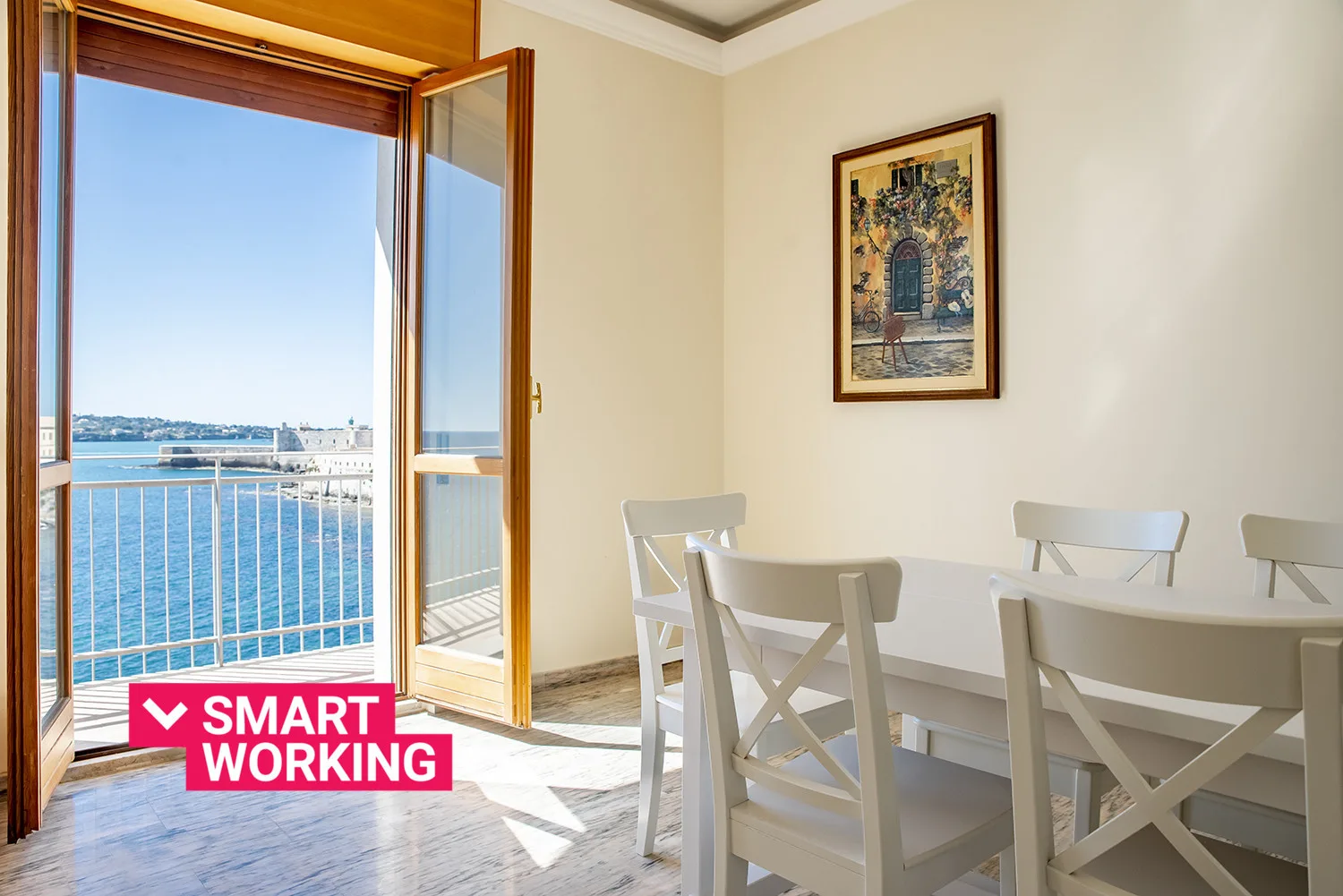 Un comedor con una mesa blanca junto a puertas abiertas con vistas al agua.