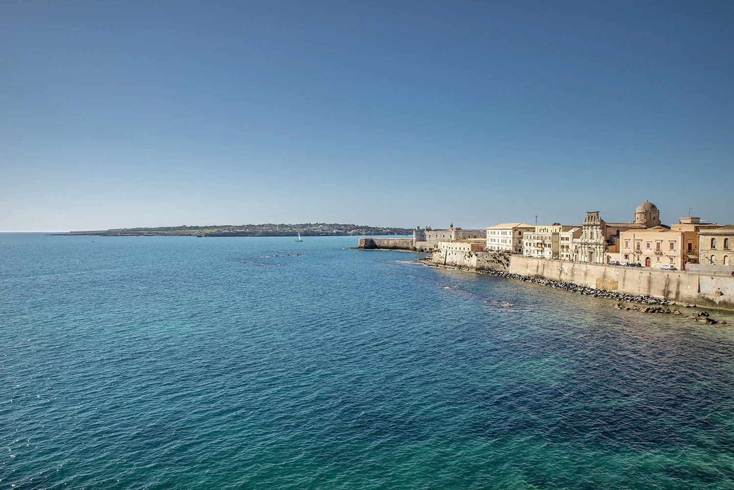 Un paseo costero con edificios históricos junto al mar azul.