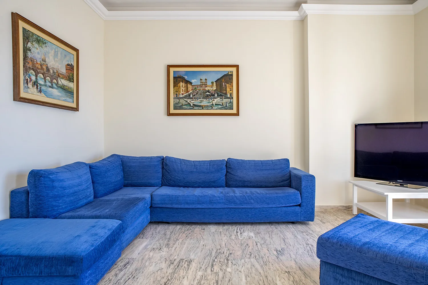 Una sala de estar con asientos azules, cuadros enmarcados y un televisor.
