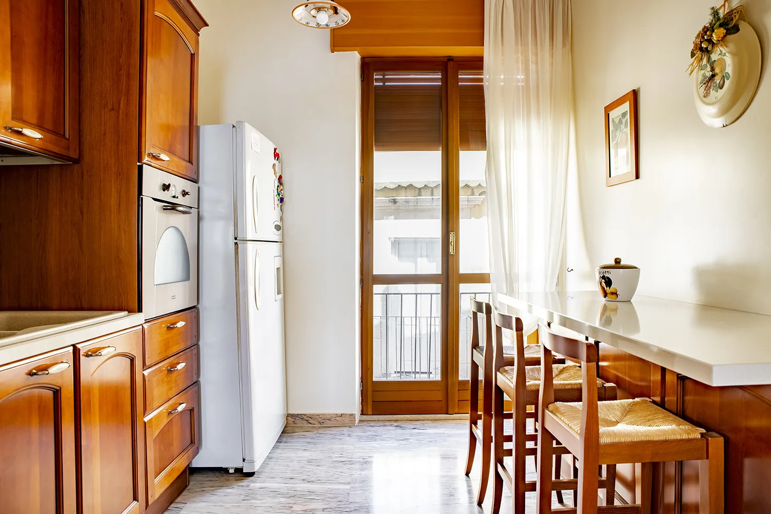 Una cocina con armarios de madera, un refrigerador y una mesa junto a la ventana.