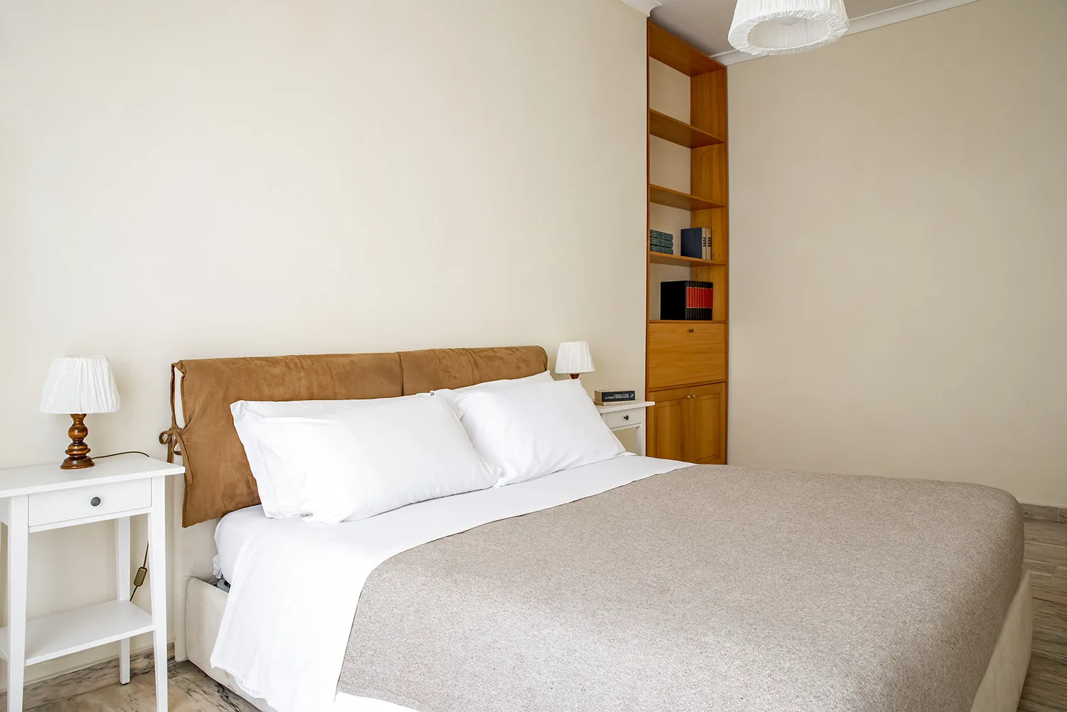 Un dormitorio con una cama bien tendida y una estantería alta de madera.