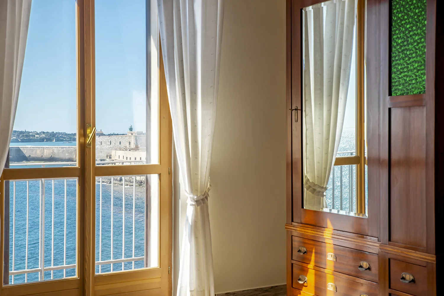 Una habitación luminosa con ventanales que dan al agua y una cómoda de madera.