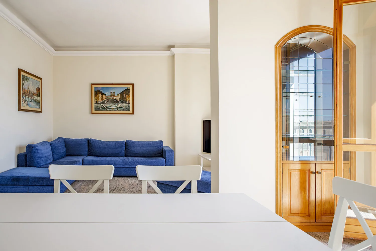 Una sala de estar con asientos azules, cuadros enmarcados y una puerta arqueada de madera.