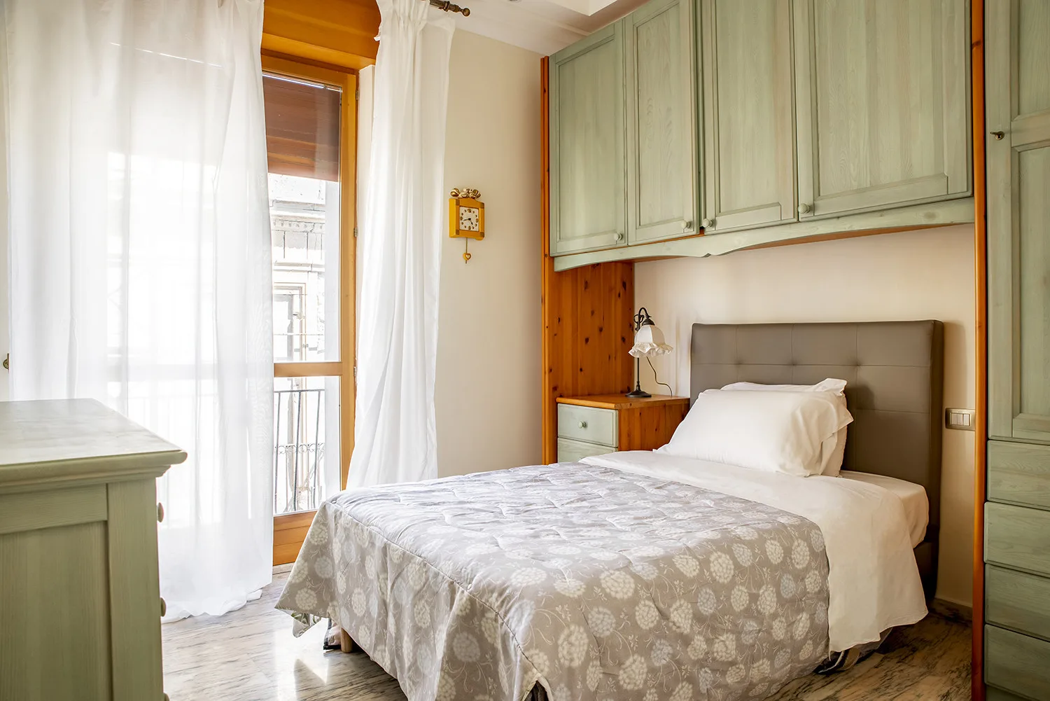 Un dormitorio con una cama bajo armarios empotrados y una ventana luminosa.