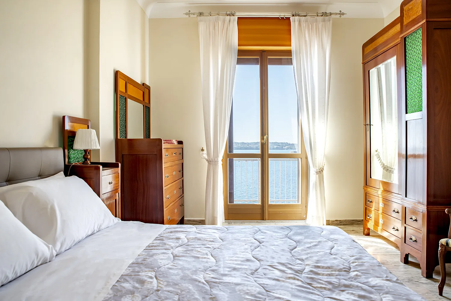 Un dormitorio con una cama y ventanas altas enmarcadas por cortinas blancas.