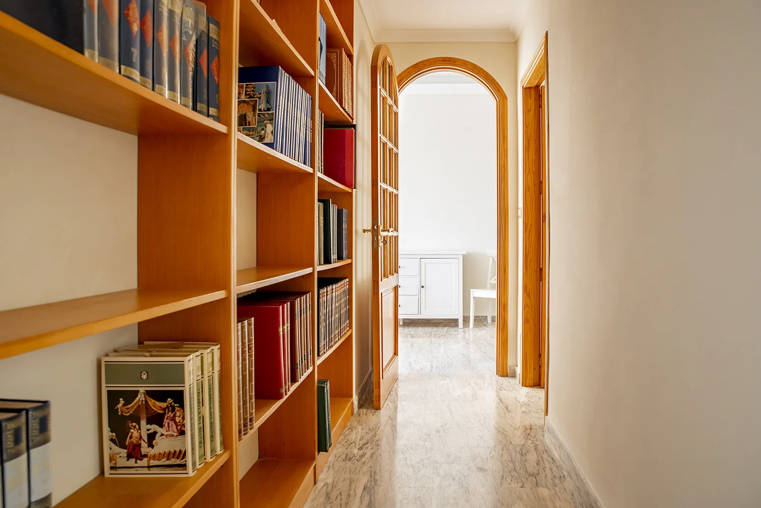 Un pasillo con estanterías de madera conduce a una habitación luminosa.