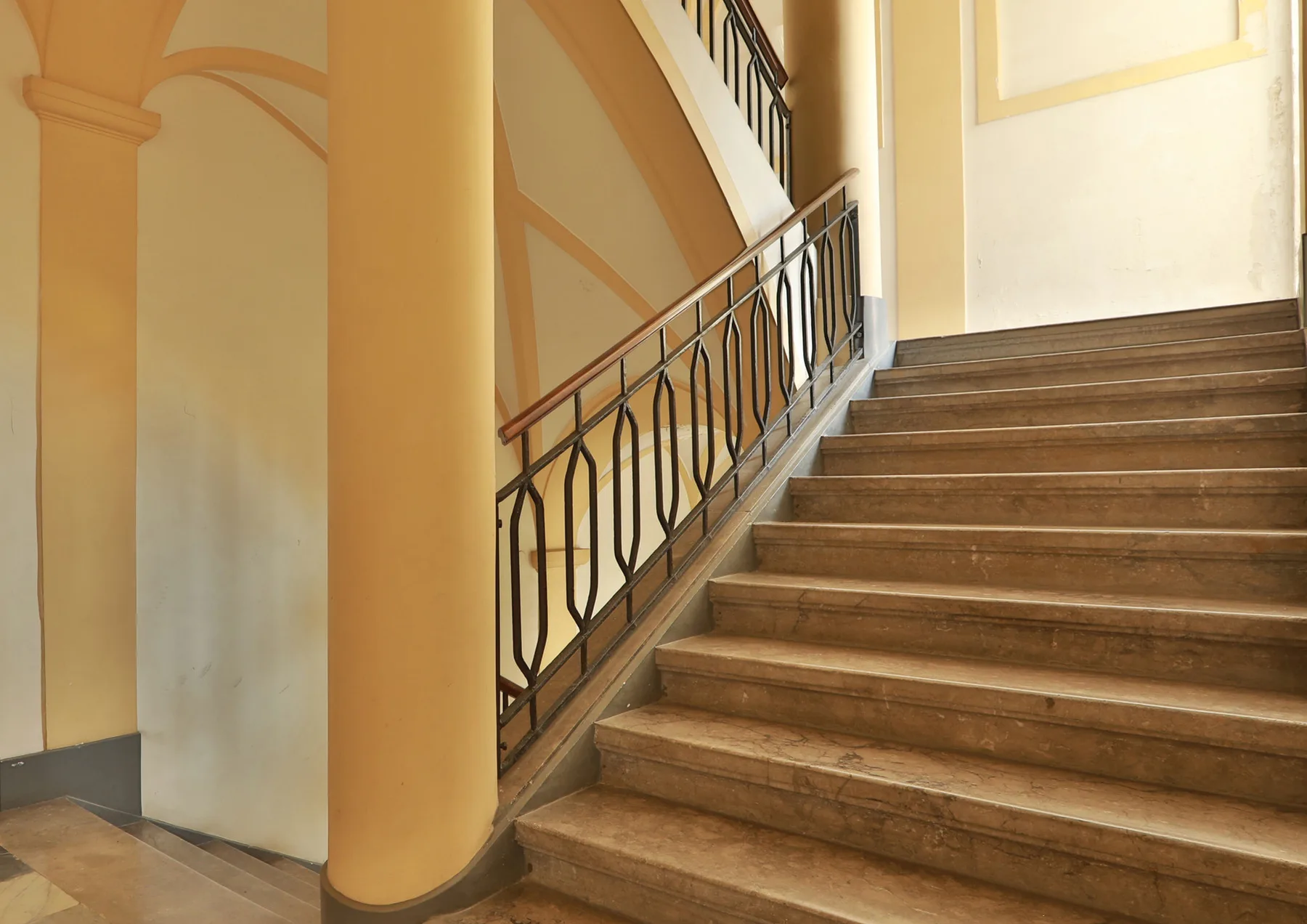 An interior staircase with broad steps and a decorative metal railing.