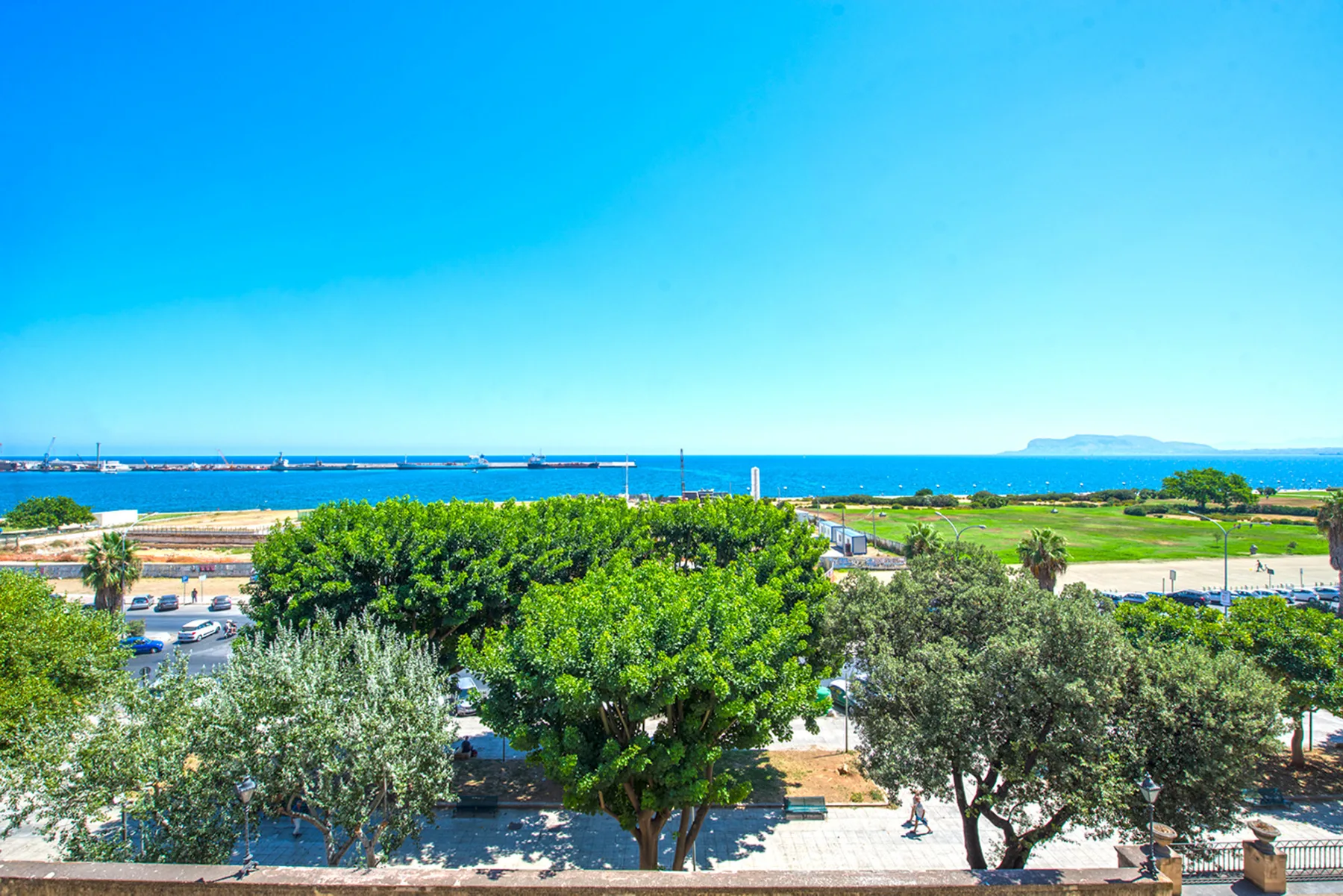 A coastal landscape with leafy trees in the foreground and the sea beyond.