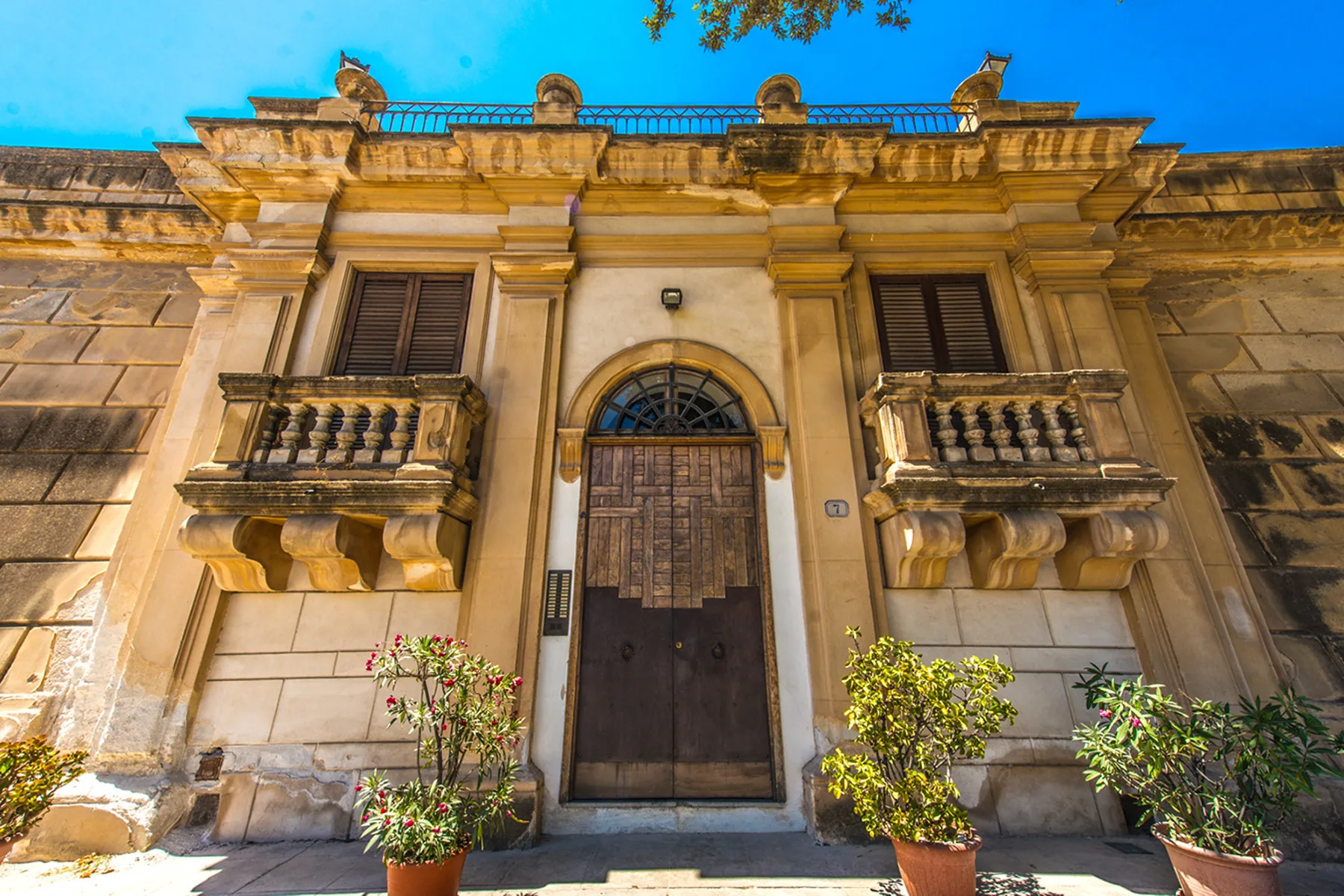 A stone building facade with a central arched wooden doorway and upper balconies.