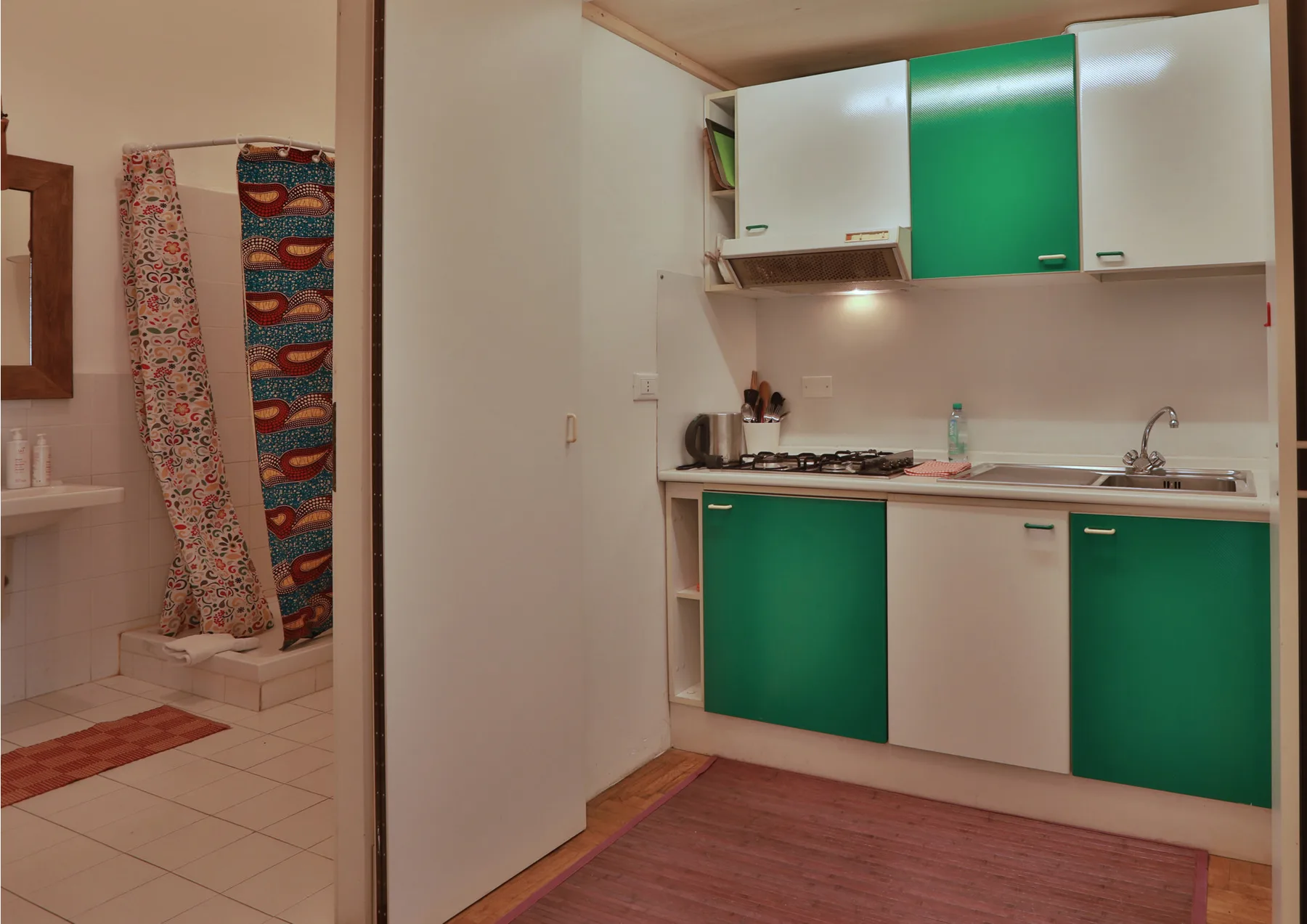 A compact kitchen with green cabinets and a countertop beside a tiled bathroom.