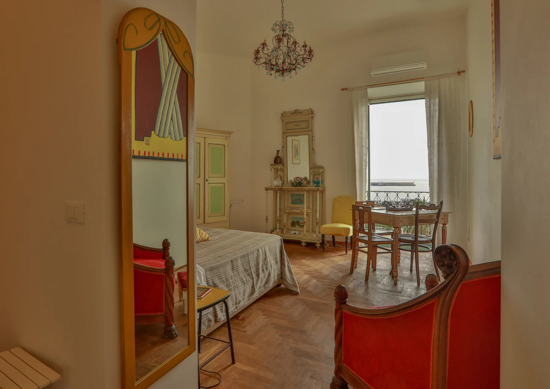 A furnished bedroom with a bed, dining table, and tall window.