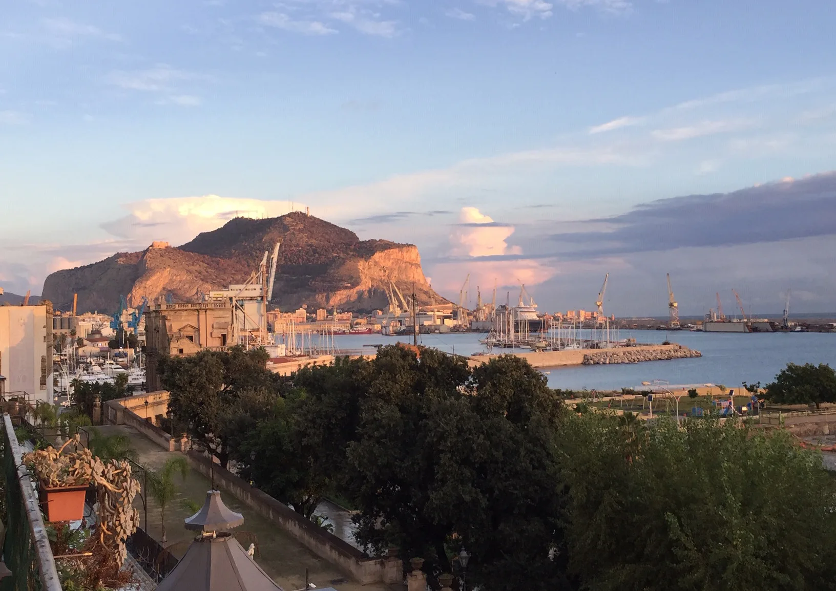 A coastal harbor and city sit beneath sunlit mountains.