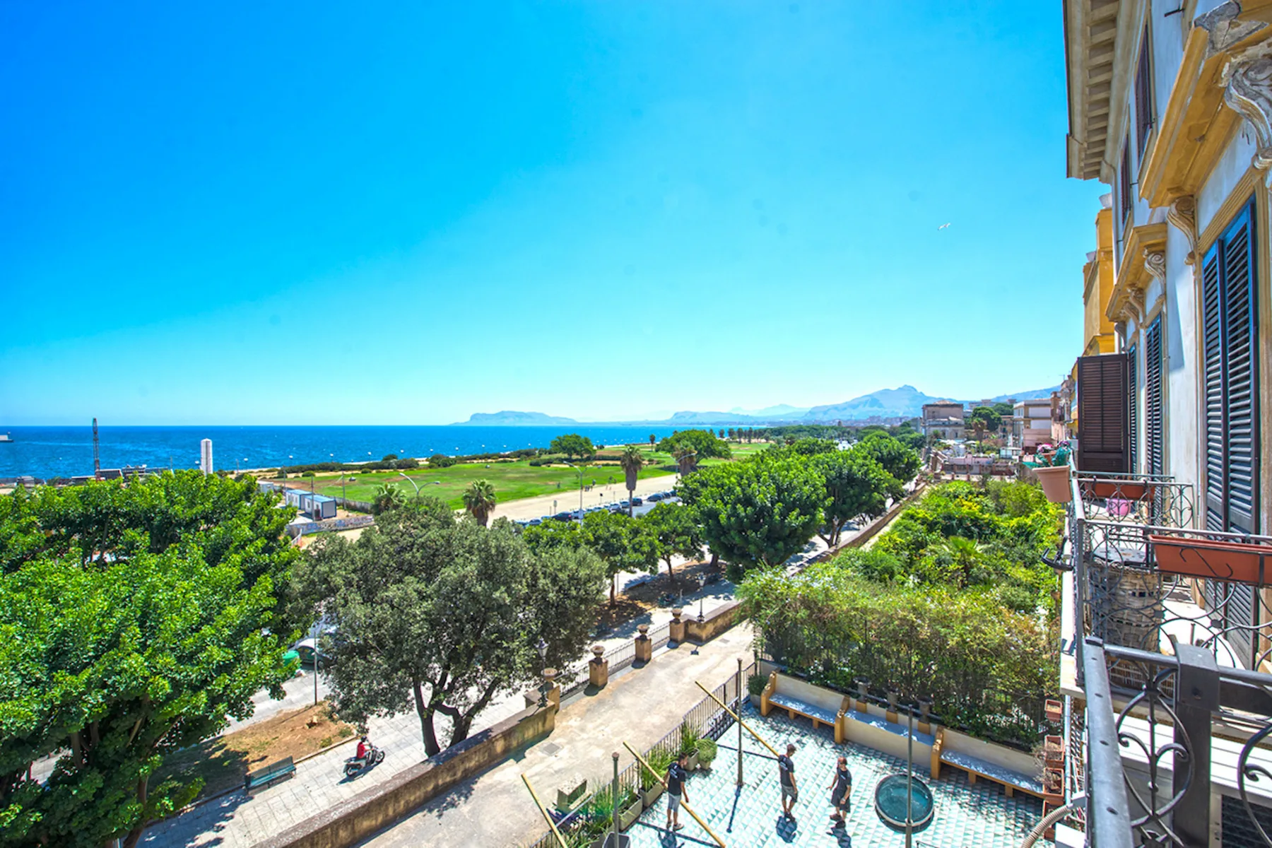 A coastal city view overlooks the sea, tree-lined streets, and nearby buildings.