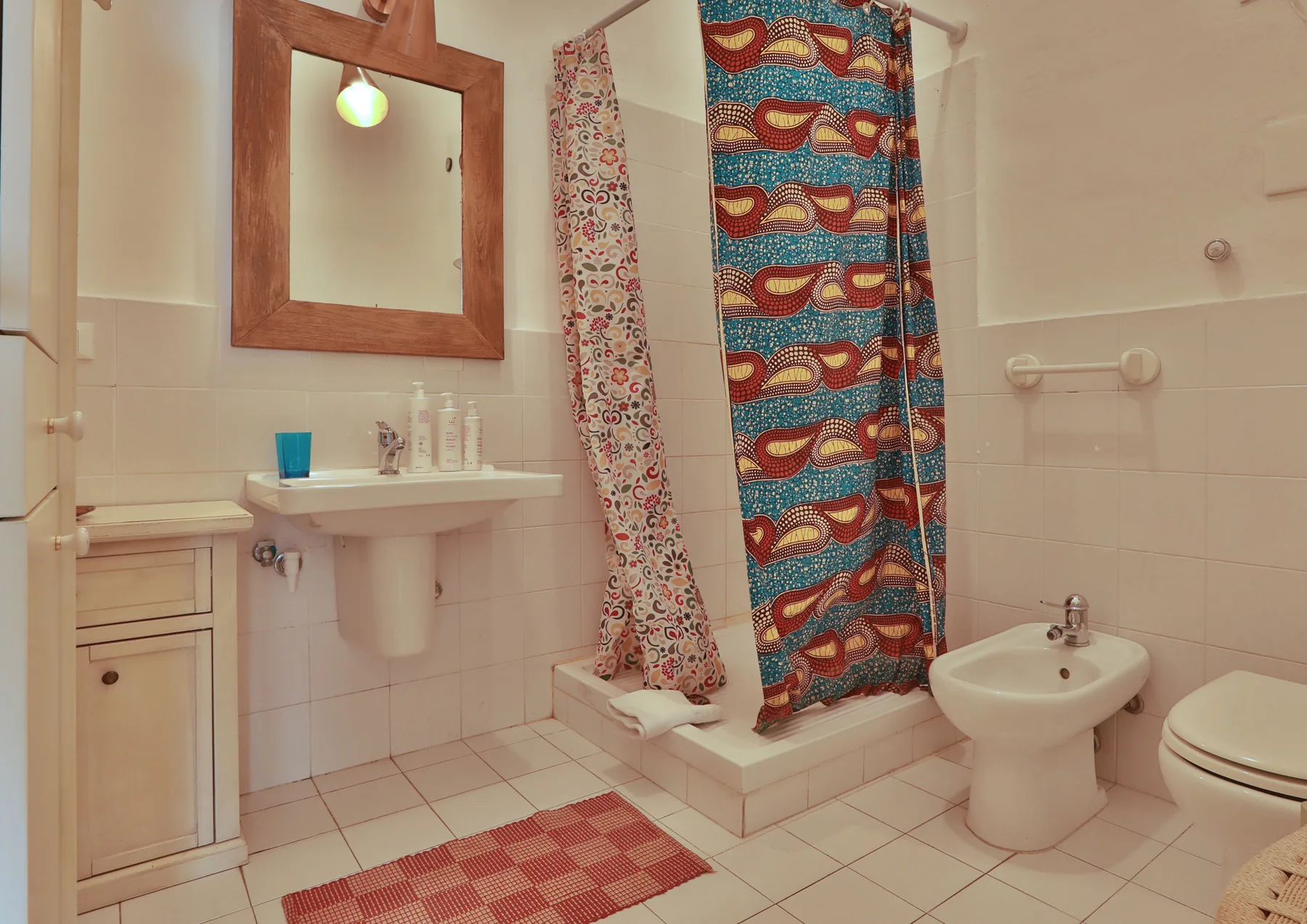 A tiled bathroom with a sink, shower curtains, and a bidet.