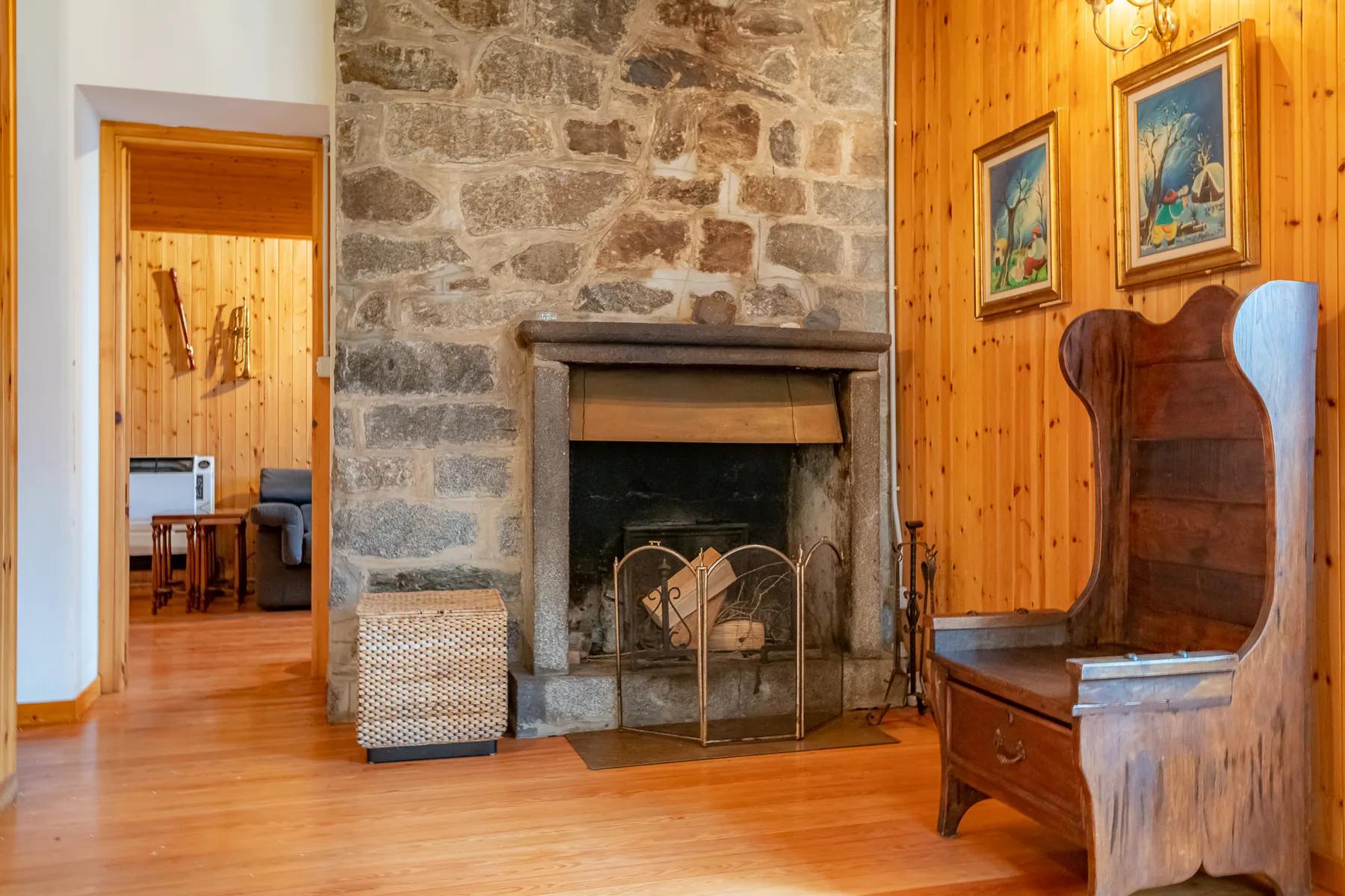Una chimenea de piedra se encuentra entre paredes revestidas de madera y una puerta abierta.