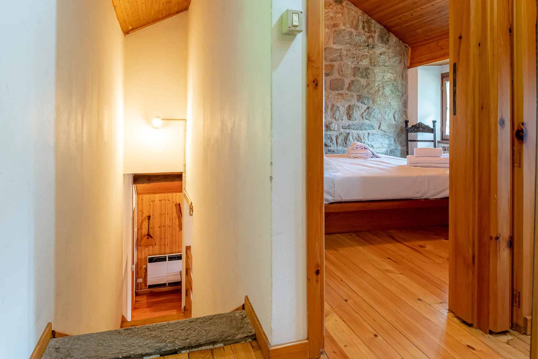 Un pasillo estrecho da a un dormitorio con una cama y una pared de piedra.