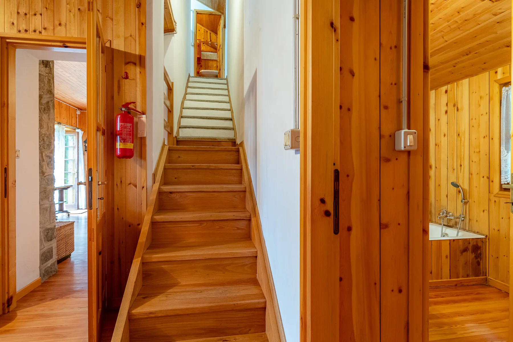 Un pasillo revestido de madera con una escalera central y puertas abiertas.