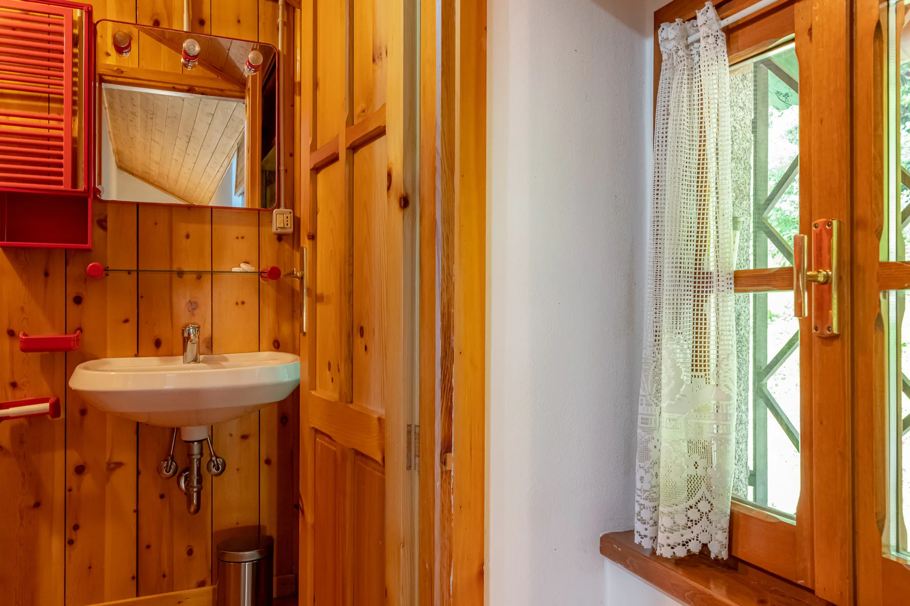 Un baño revestido de madera con un lavabo suspendido y una ventana con cortina.