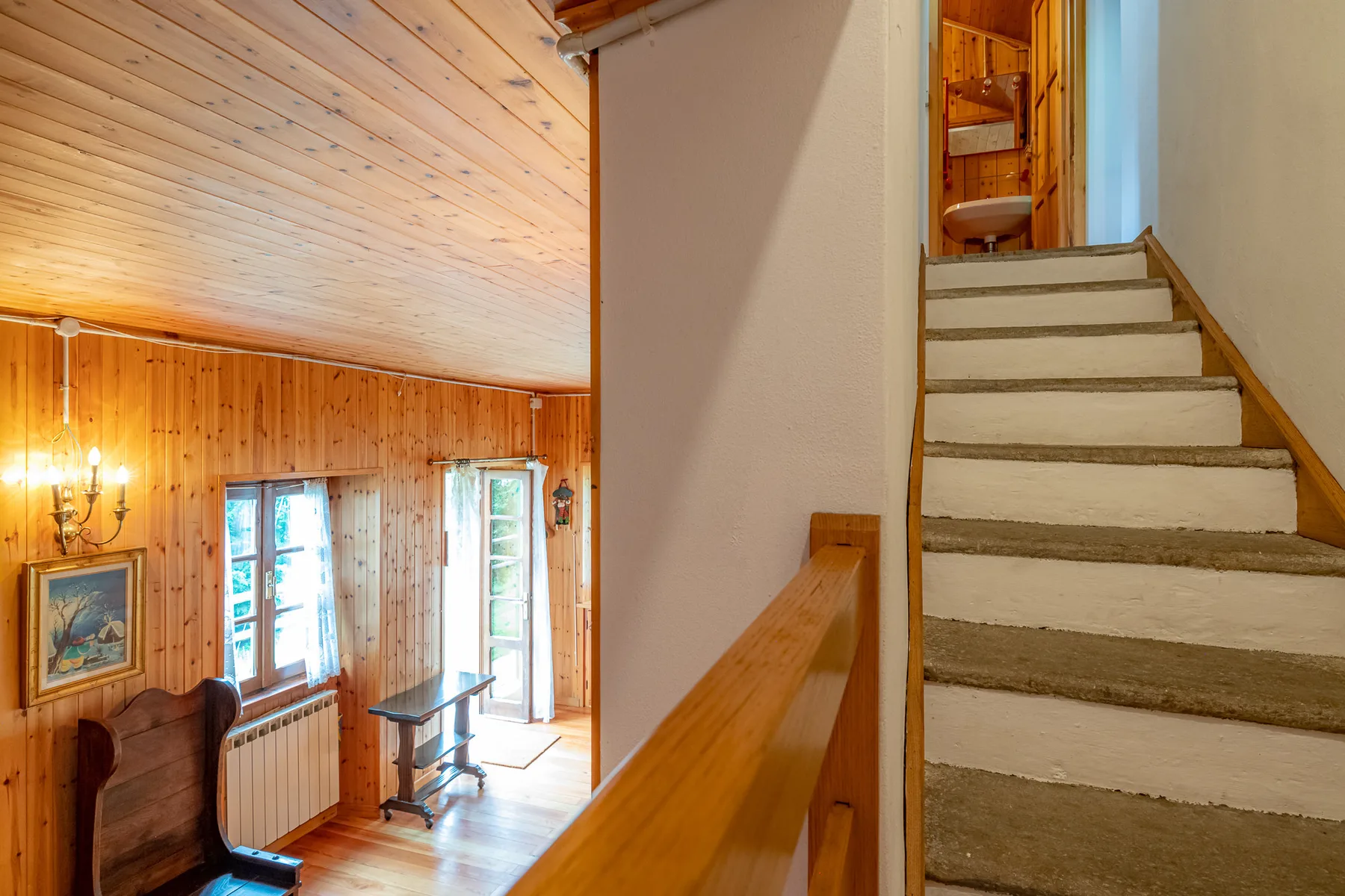 Un interior revestido de madera con una escalera junto a una habitación iluminada por el sol.