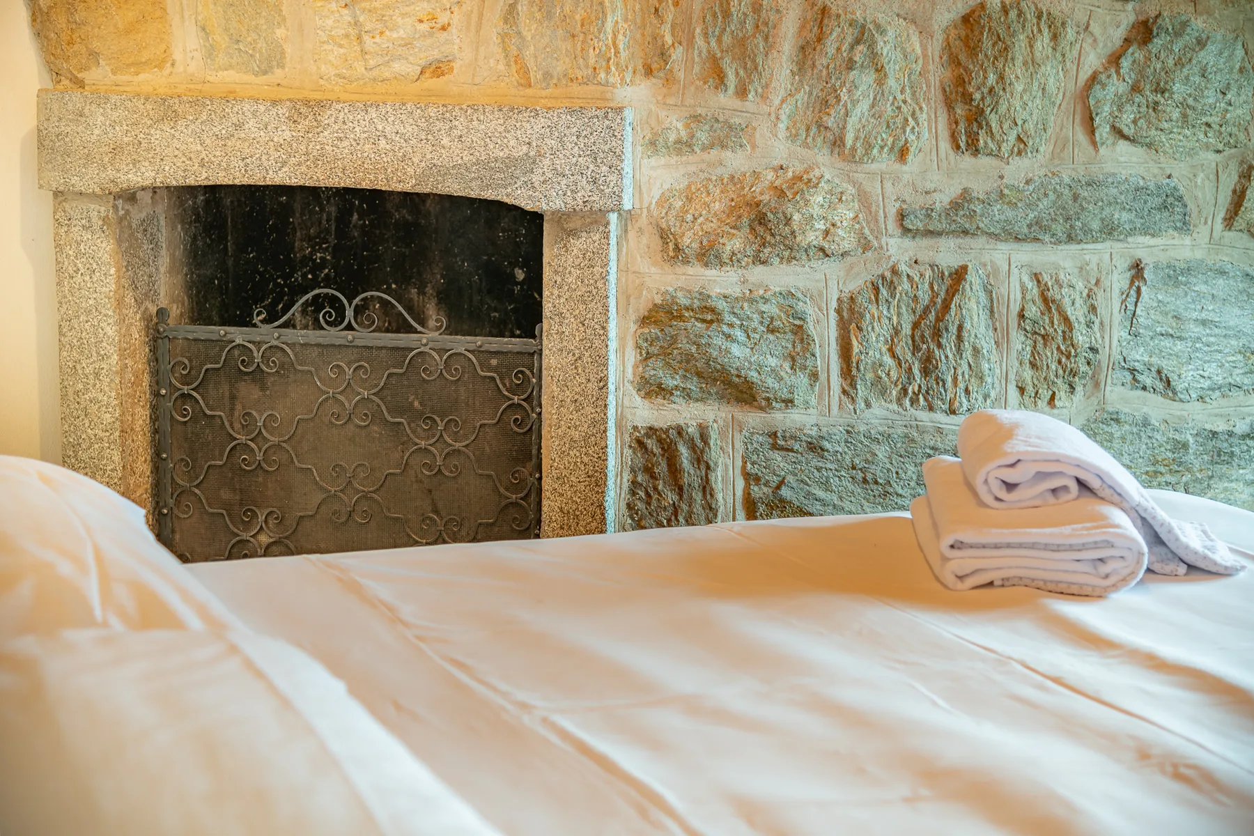 Un dormitorio con una chimenea de piedra y toallas dobladas sobre la cama.