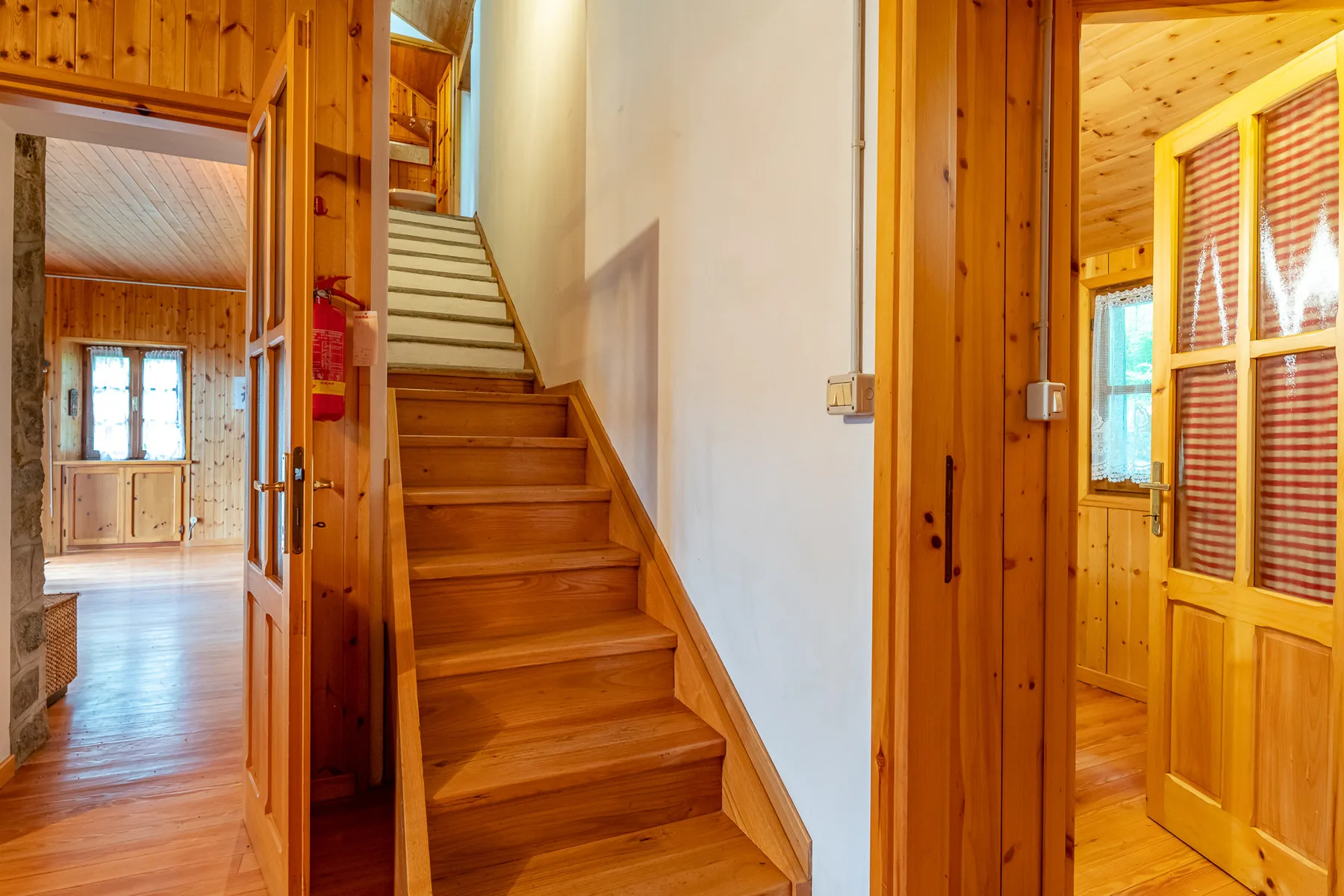 Una escalera de madera sube entre un pasillo y habitaciones contiguas.