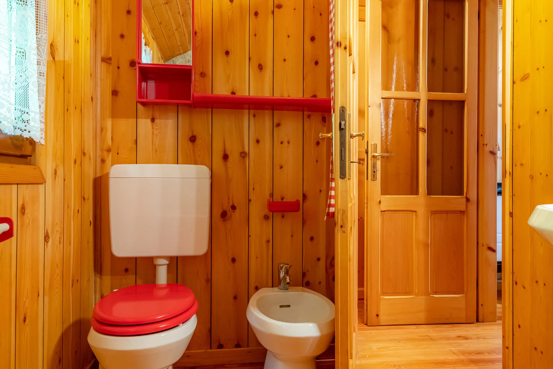 Un baño revestido de madera con inodoro, bidé y una puerta abierta.