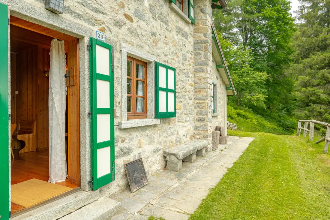 La entrada de un edificio de piedra da a un patio con césped y contraventanas verdes.