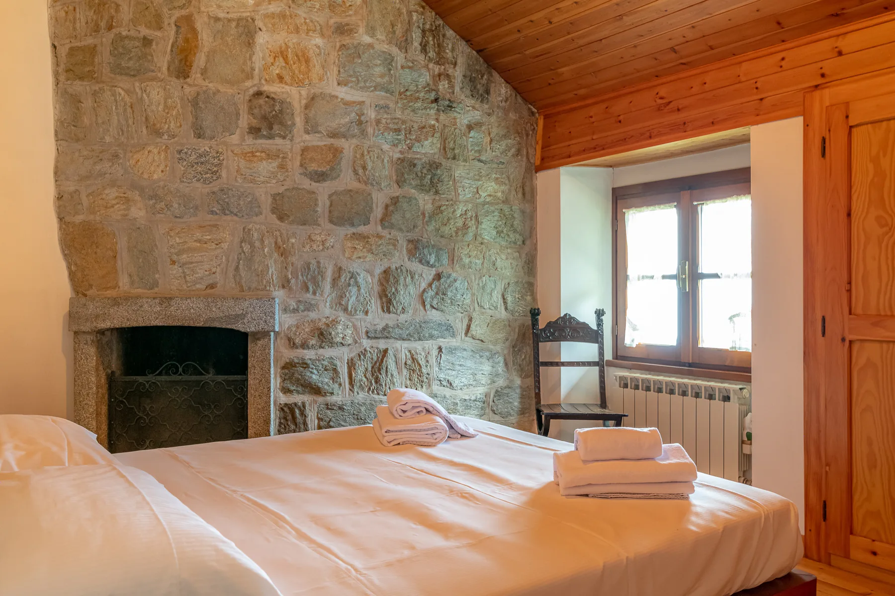 Un dormitorio con una cama junto a una chimenea de piedra y una ventana luminosa.