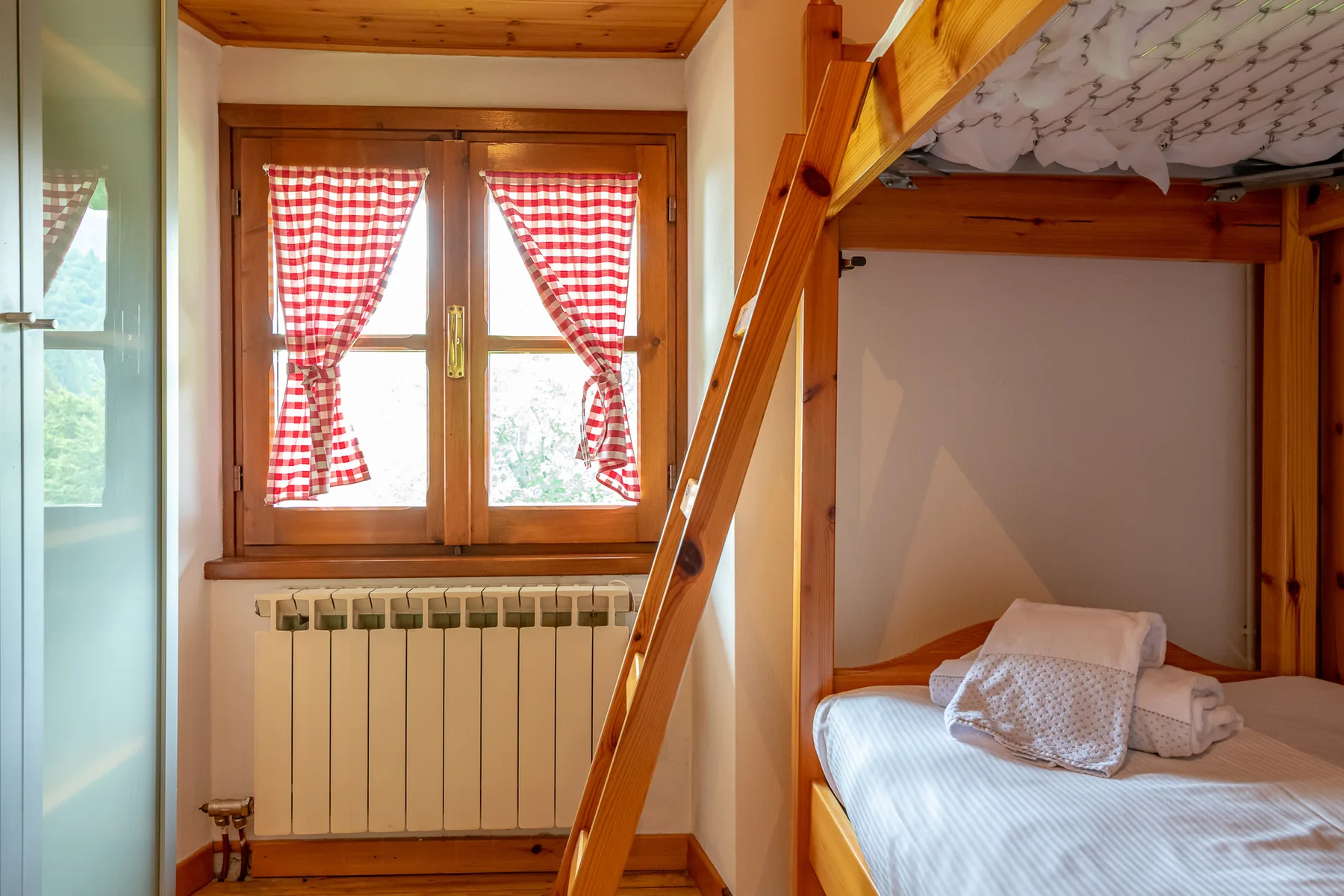 Un dormitorio con una litera de madera y una ventana con cortinas rojas y blancas.
