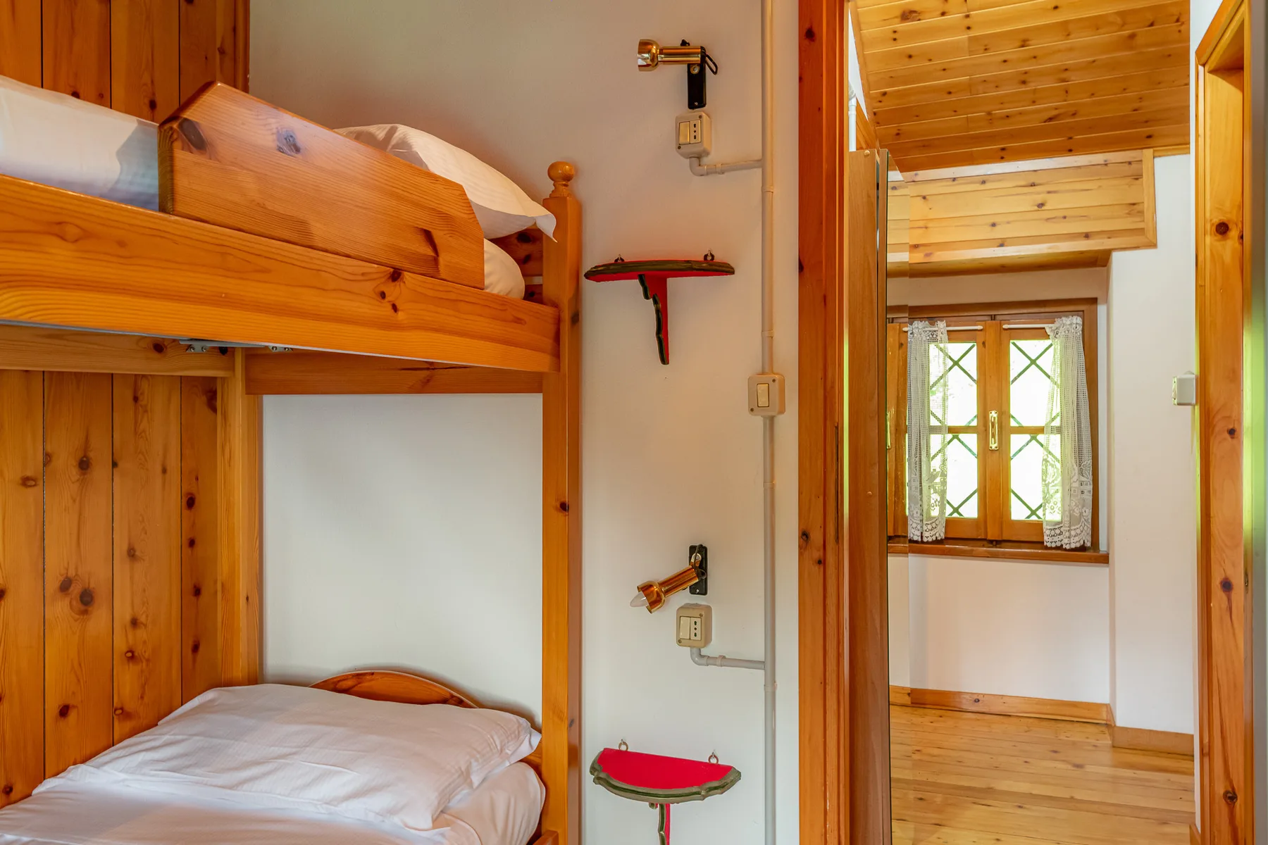 Una litera de madera junto a una puerta abierta hacia una habitación luminosa.