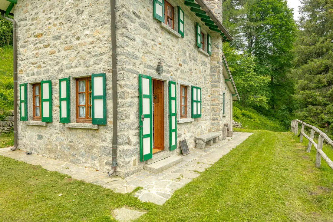 Una casa de piedra con ventanas de marco verde junto a un sendero con césped.