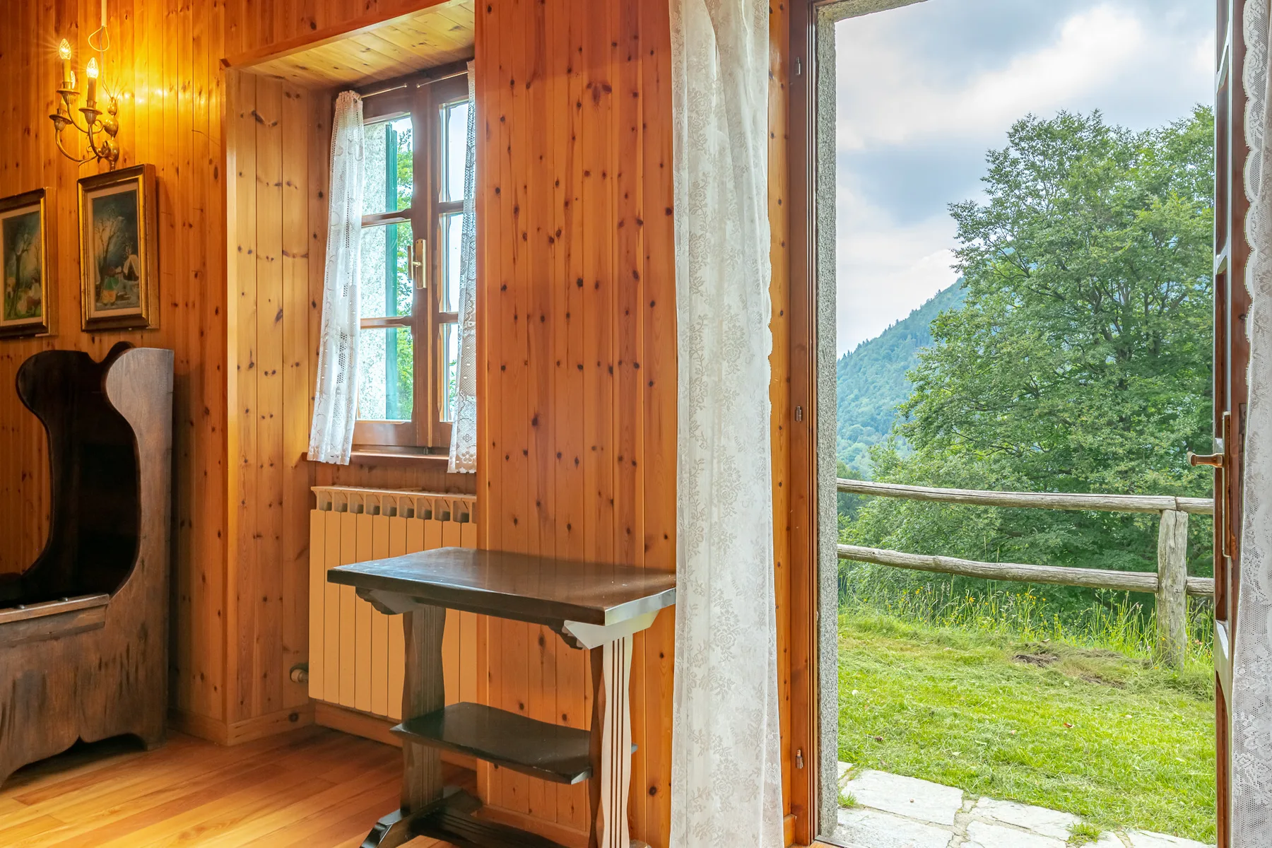 Una habitación revestida de madera da a un paisaje verde a través de una puerta.