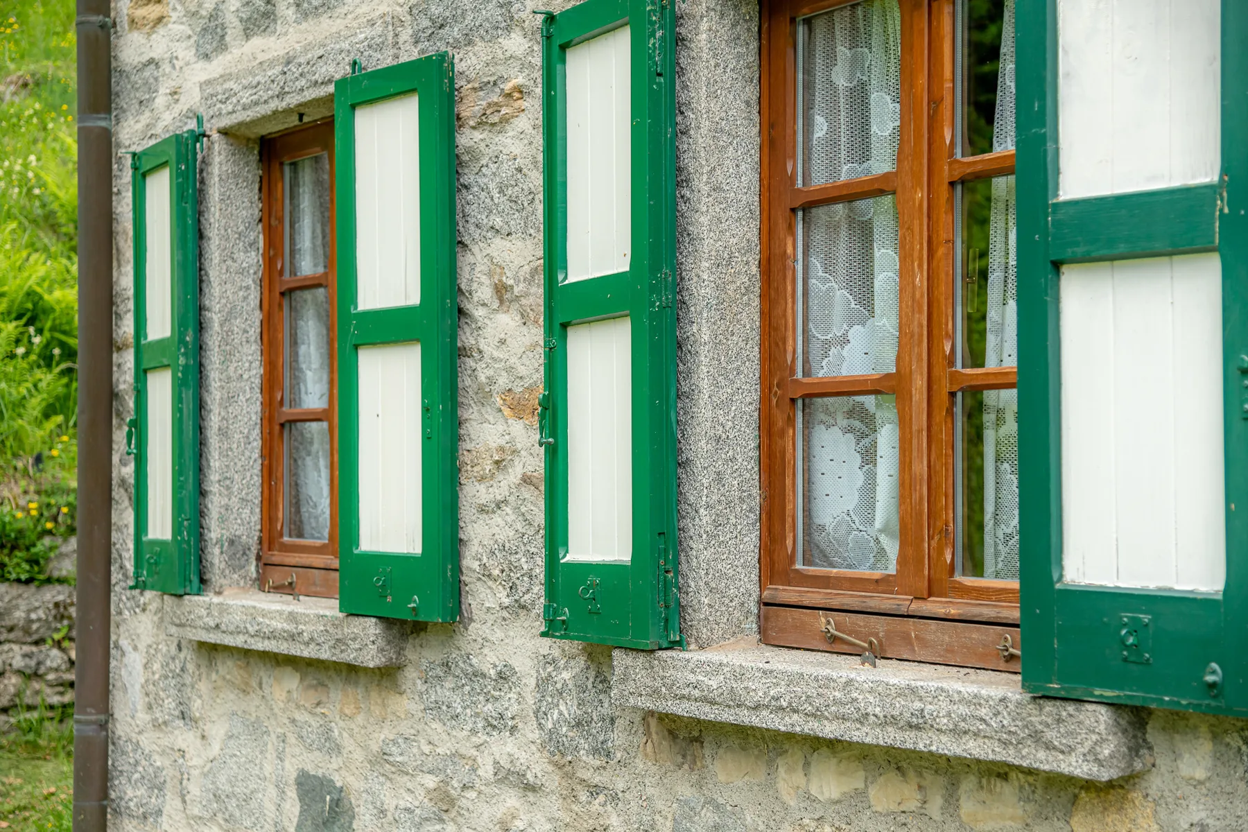 Una fachada de piedra con ventanas de madera y contraventanas verdes abiertas.