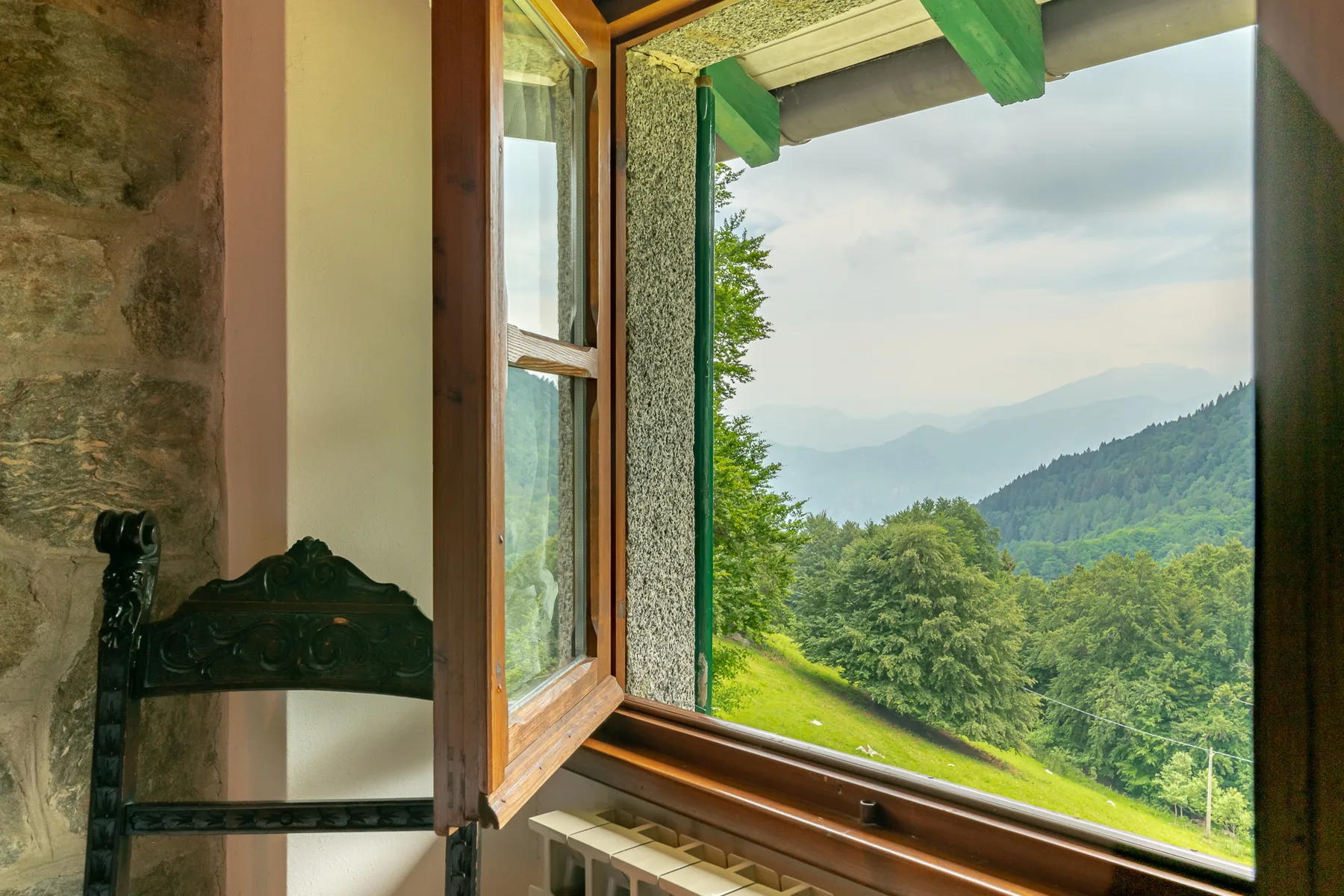 Una ventana abierta ofrece vistas de colinas verdes y montañas lejanas.