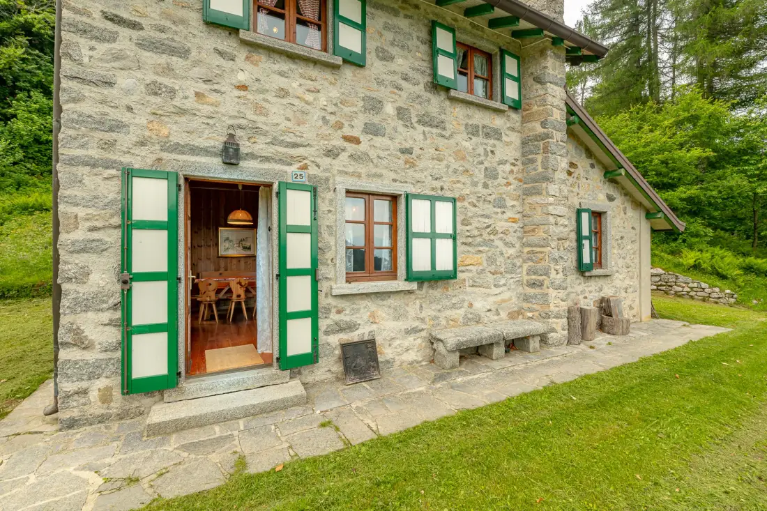 A stone house with green shutters stands beside a grassy lawn.