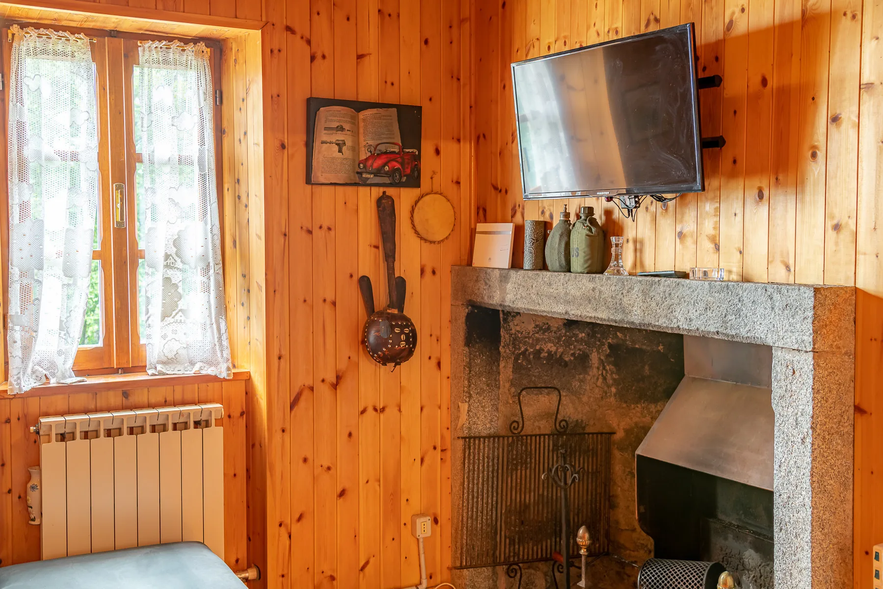 Una habitación revestida de madera con chimenea, televisor en la pared y ventana con cortinas.