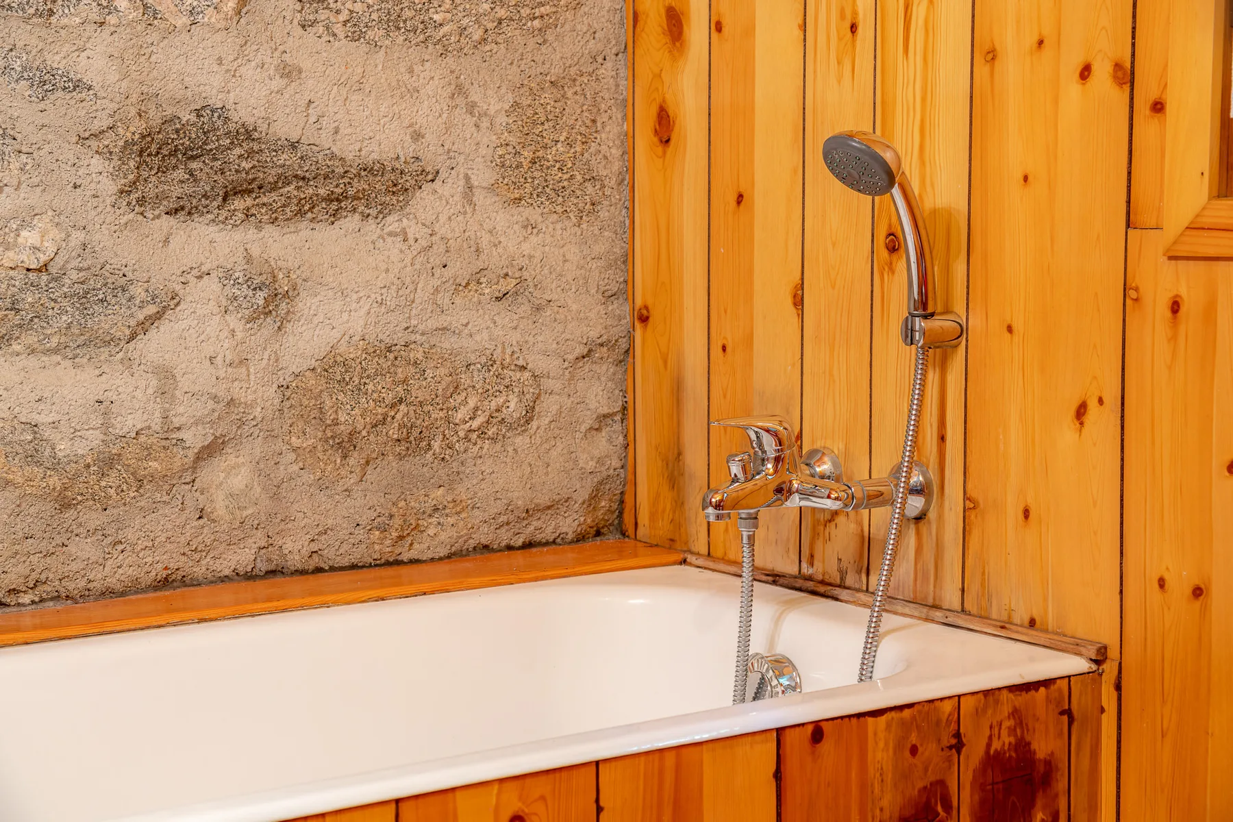 Una bañera con ducha de pared está junto a una pared de piedra texturizada.