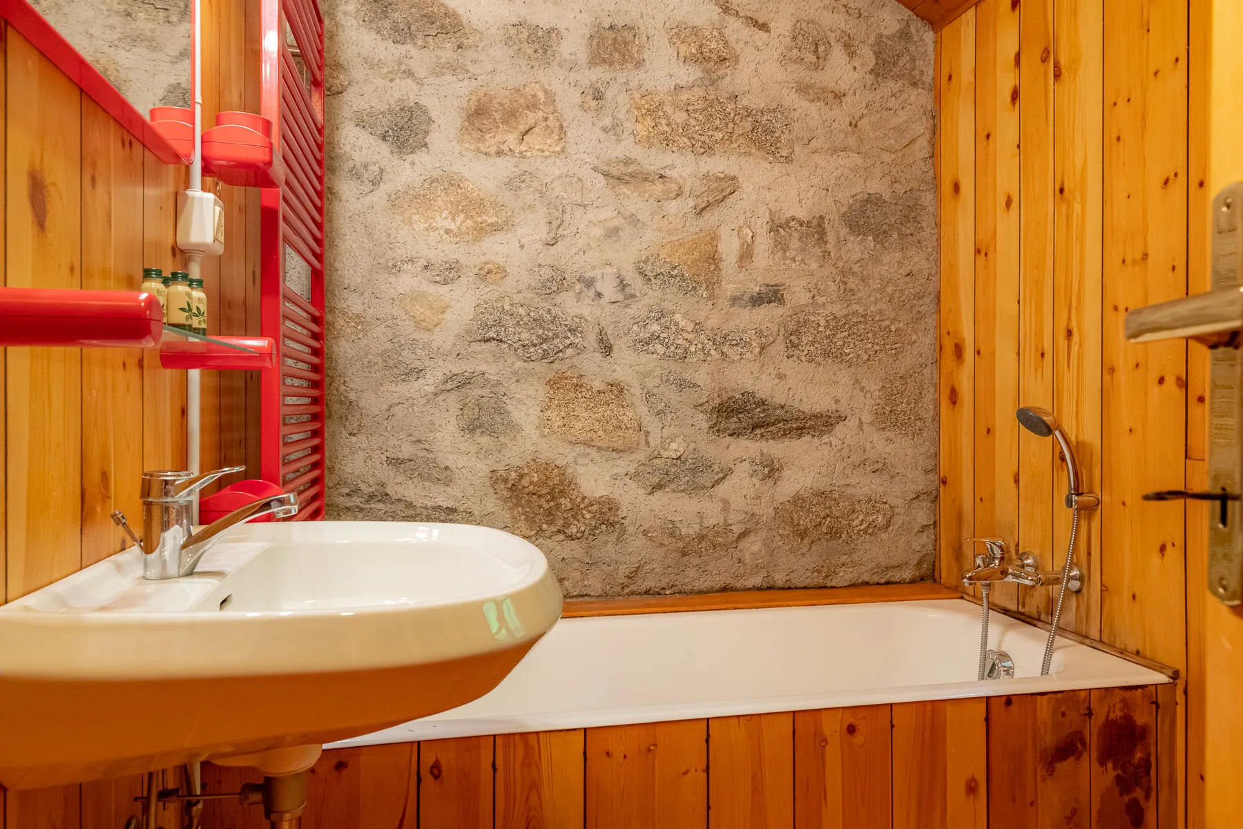 Un baño con bañera, lavabo y una pared de piedra.